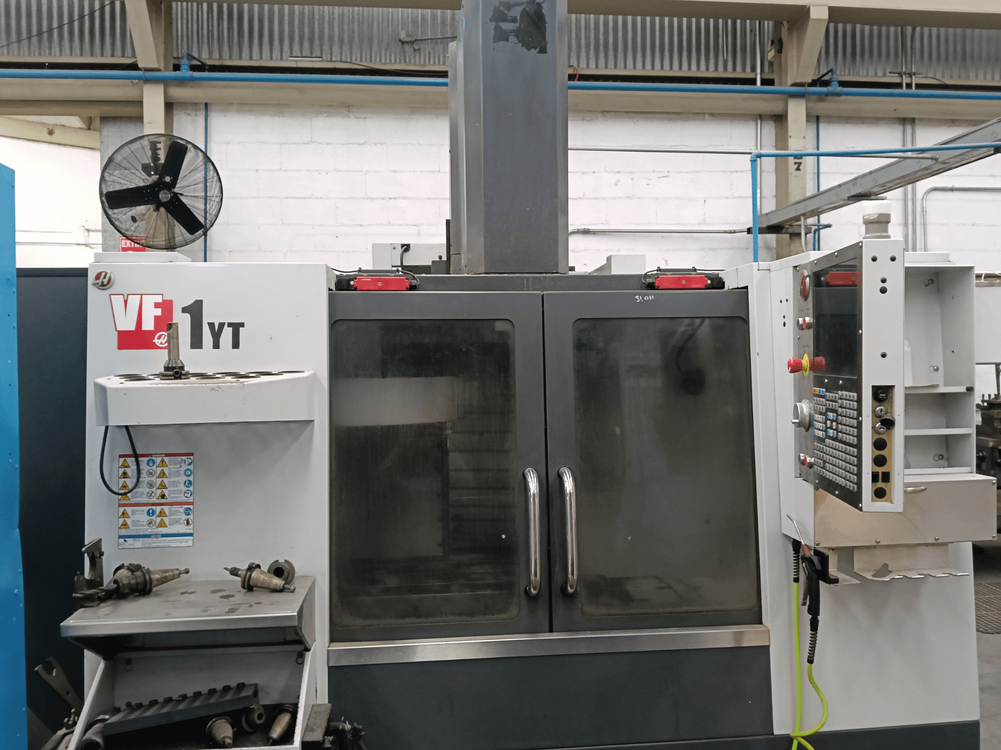 Vorderansicht des vertikalen Bearbeitungszentrums HAAS VF-1YT-1 mit Bedienfeld und Werkzeugen an der Seite.