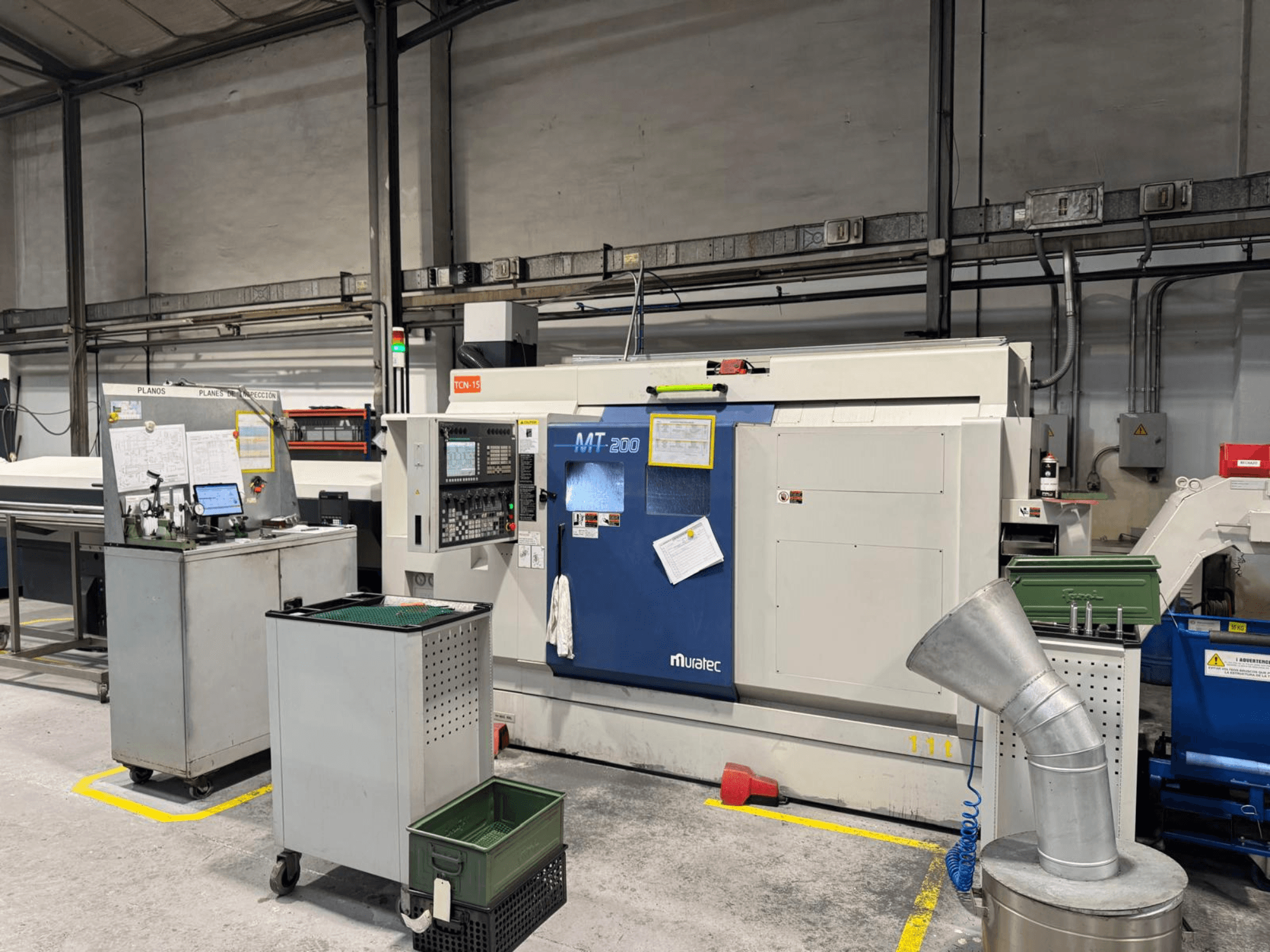 Muratec MT200 Mehrspindeldrehmaschine in einer Werksumgebung, von vorne gesehen, mit Bedienfeld und umliegenden Geräten.