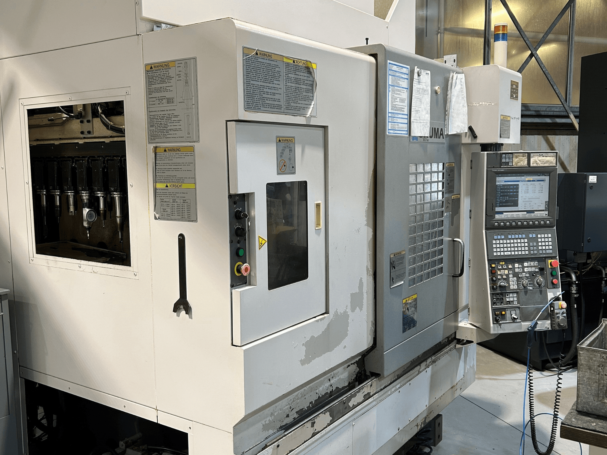 Frontansicht einer UMA CNC-Maschine mit sichtbaren Werkzeughaltern, Bedienfeld, Warnschildern und Bedientasten.