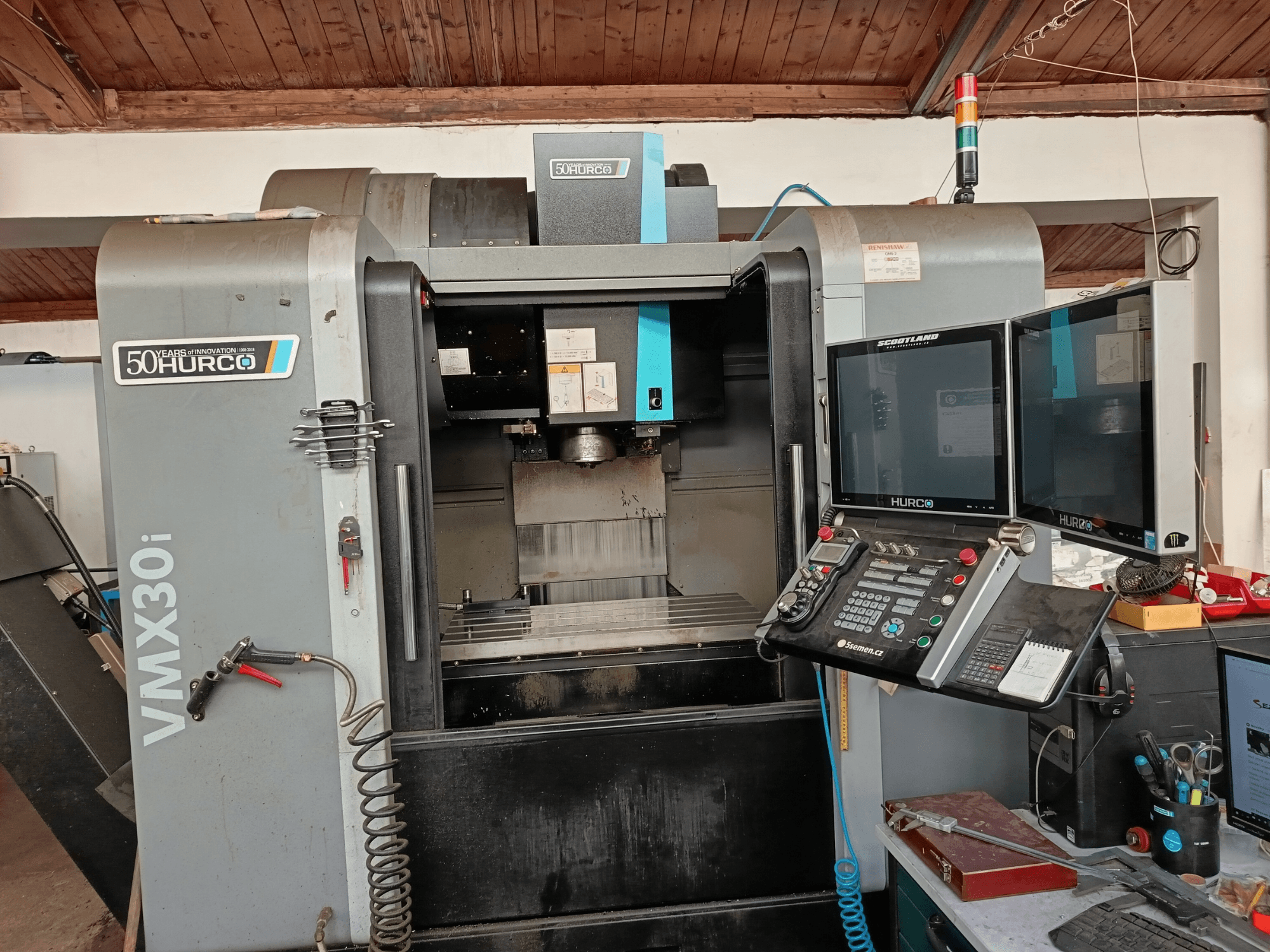 Hurco VMX30i CNC-Fräsmaschine in der Vorderansicht, mit zwei Monitoren, Bedienfeld und einem Schlauch.