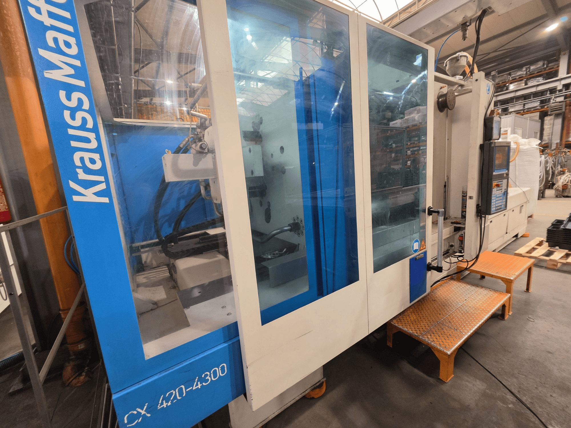 Hydraulische Spritzgießmaschine Krauss Maffei CX 420-4300, Seitenansicht mit Bedienpult und Klarsichttafeln.
