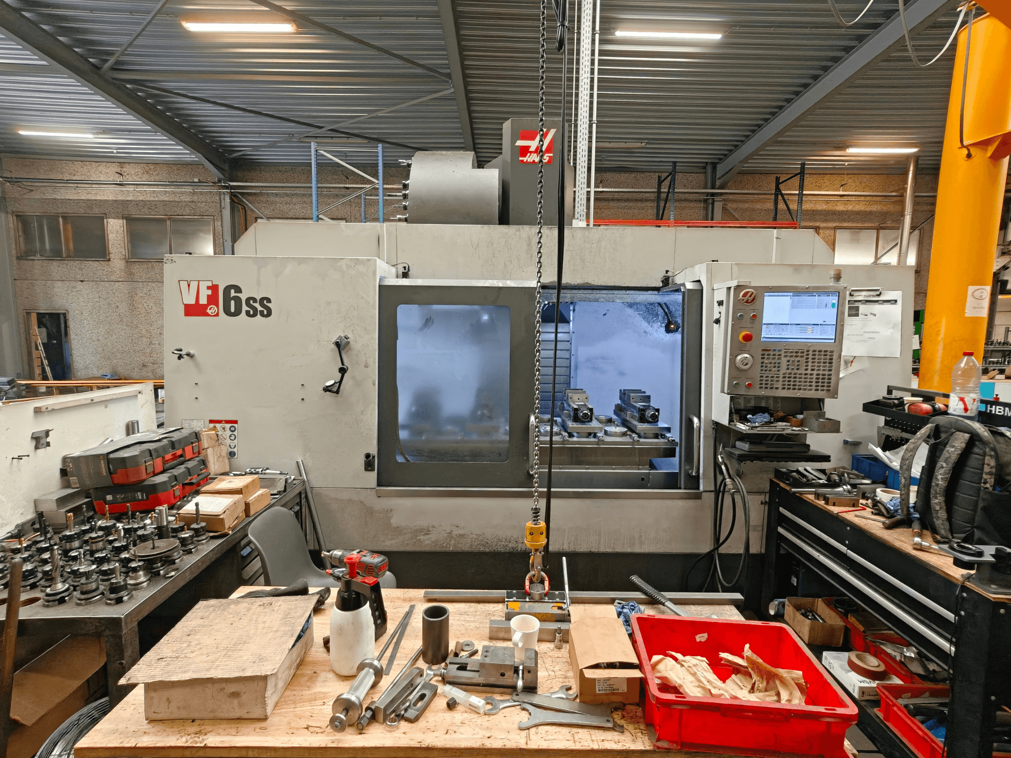 Vertikales Bearbeitungszentrum Haas VF-6SS in einer Werkstatt, Seitenansicht mit Blick auf das Bedienfeld und den mit Werkzeugen übersäten Arbeitsbereich.