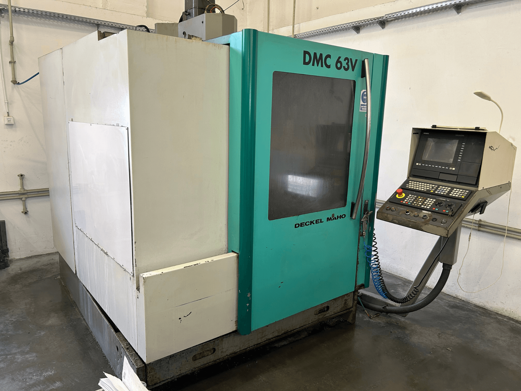 Vertikales Bearbeitungszentrum DECKEL MAHO DMC 63V in der Frontansicht mit Bedienfeld und blau-grünem Gehäuse.
