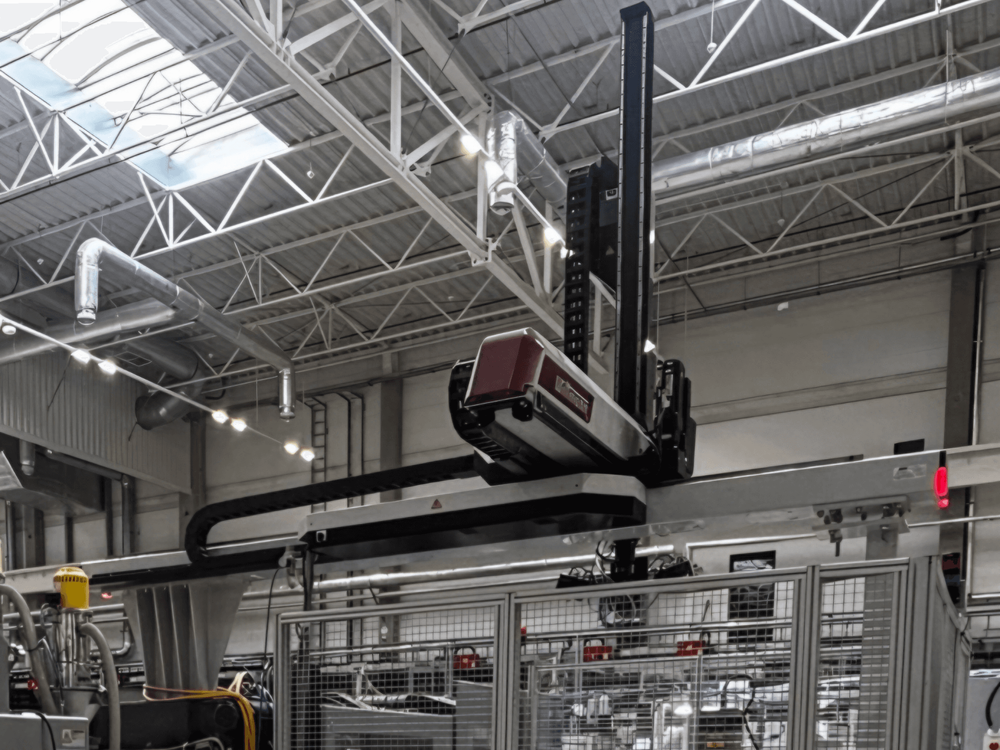 WITTMANN W832PRO Kunststoffverarbeitungsmaschine in einer Fabrikumgebung, Seitenansicht mit Blick auf das Überkopf-System und den industriellen Hintergrund.