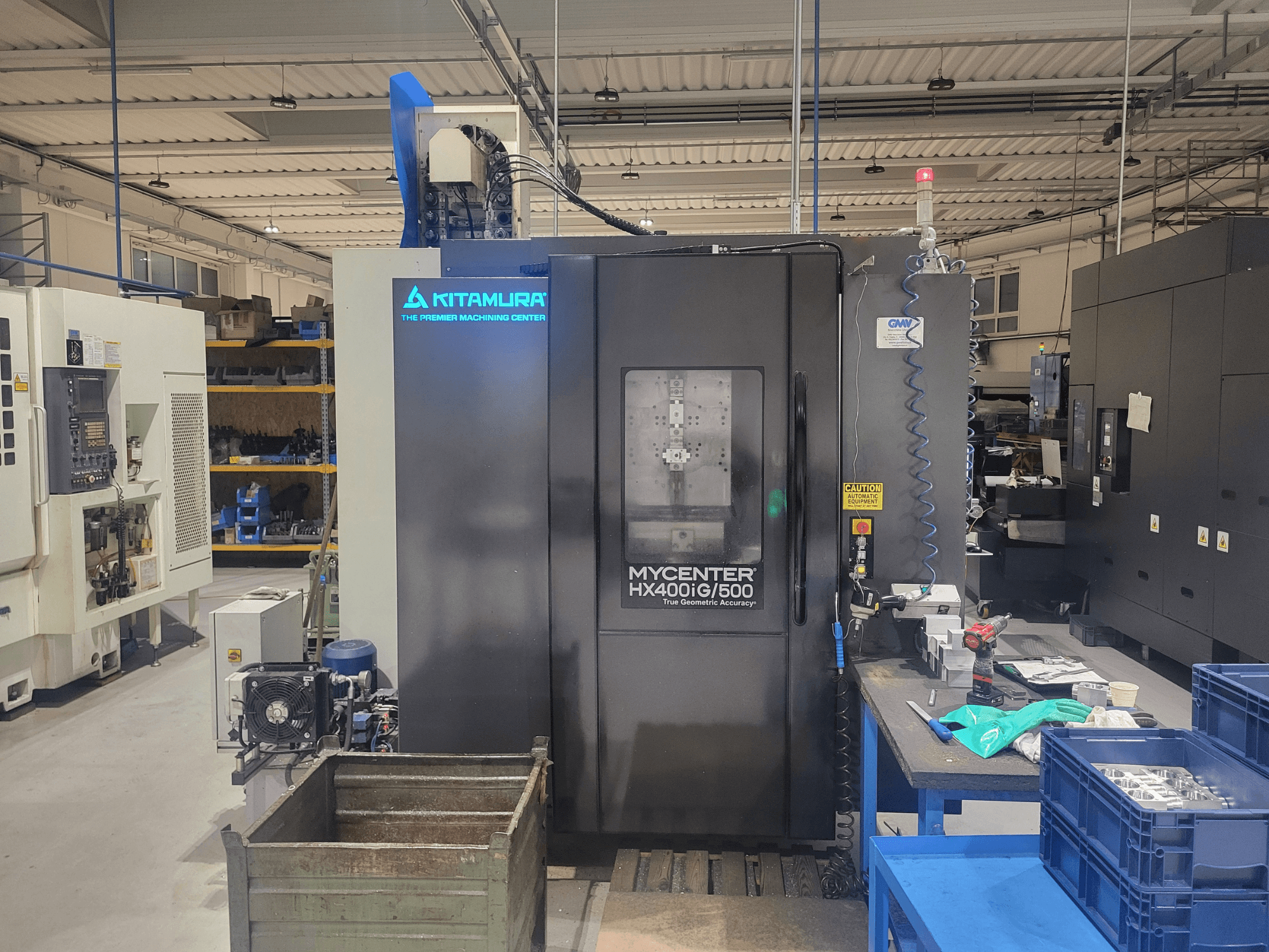 Kitamura Mycenter HX400iG/500 CNC-Maschine in einer Werkstatt, Vorderansicht, mit Steuerungen, Werkzeugablage und Materialien in der Nähe.