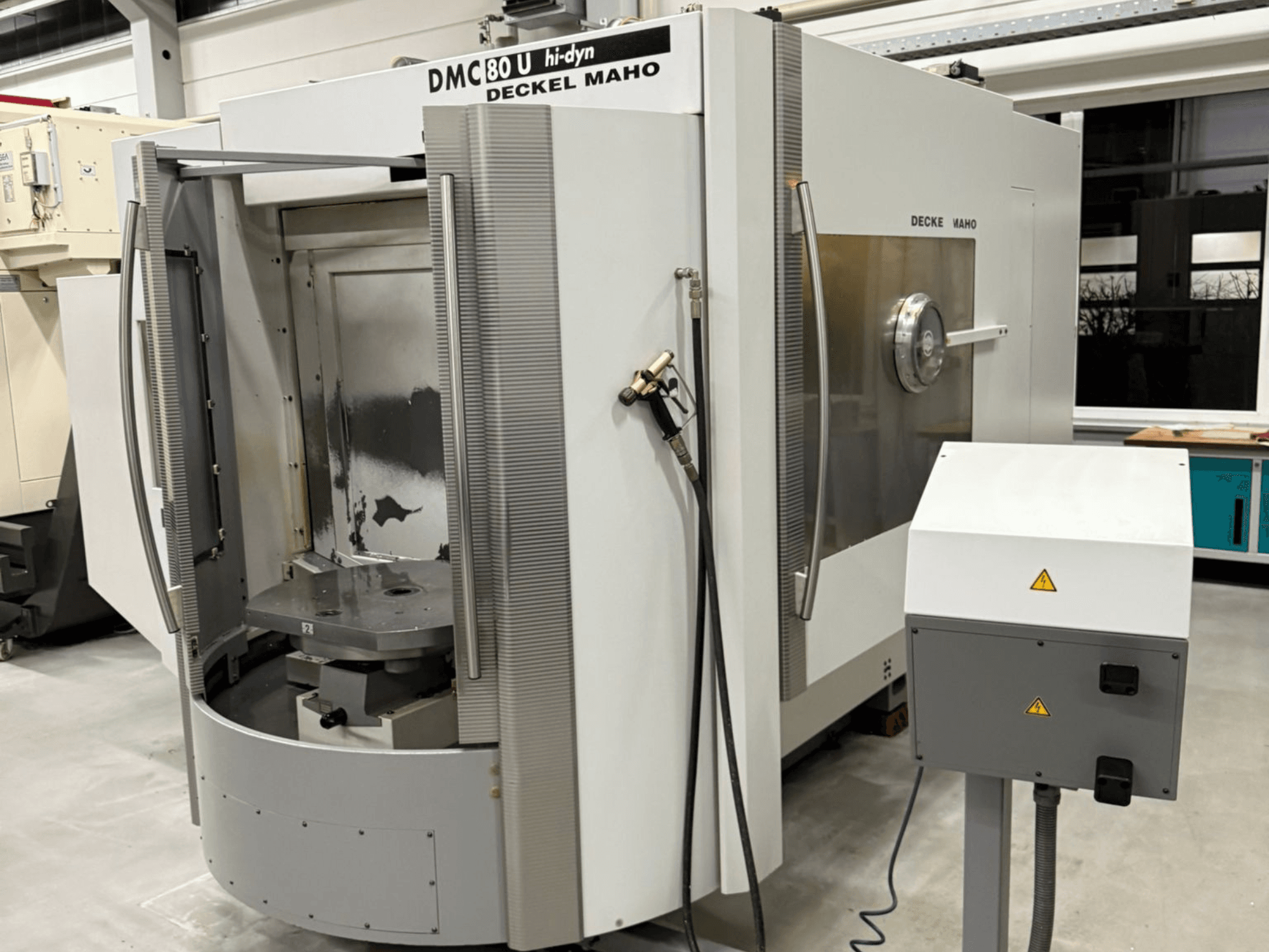 Vorderansicht einer CNC-Maschine DECKEL MAHO DMC 80 U mit geöffneten Türen, die den Arbeitsbereich und das Bedienfeld zeigen, in einer Fabrikumgebung.