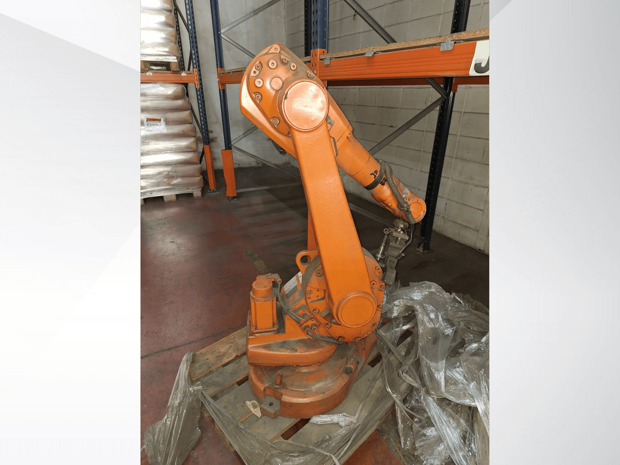 Industrieller Roboterarm in Orange, Vorderansicht auf einer Holzpalette, mit befestigtem Kabel und Schutzfolie um die Basis.