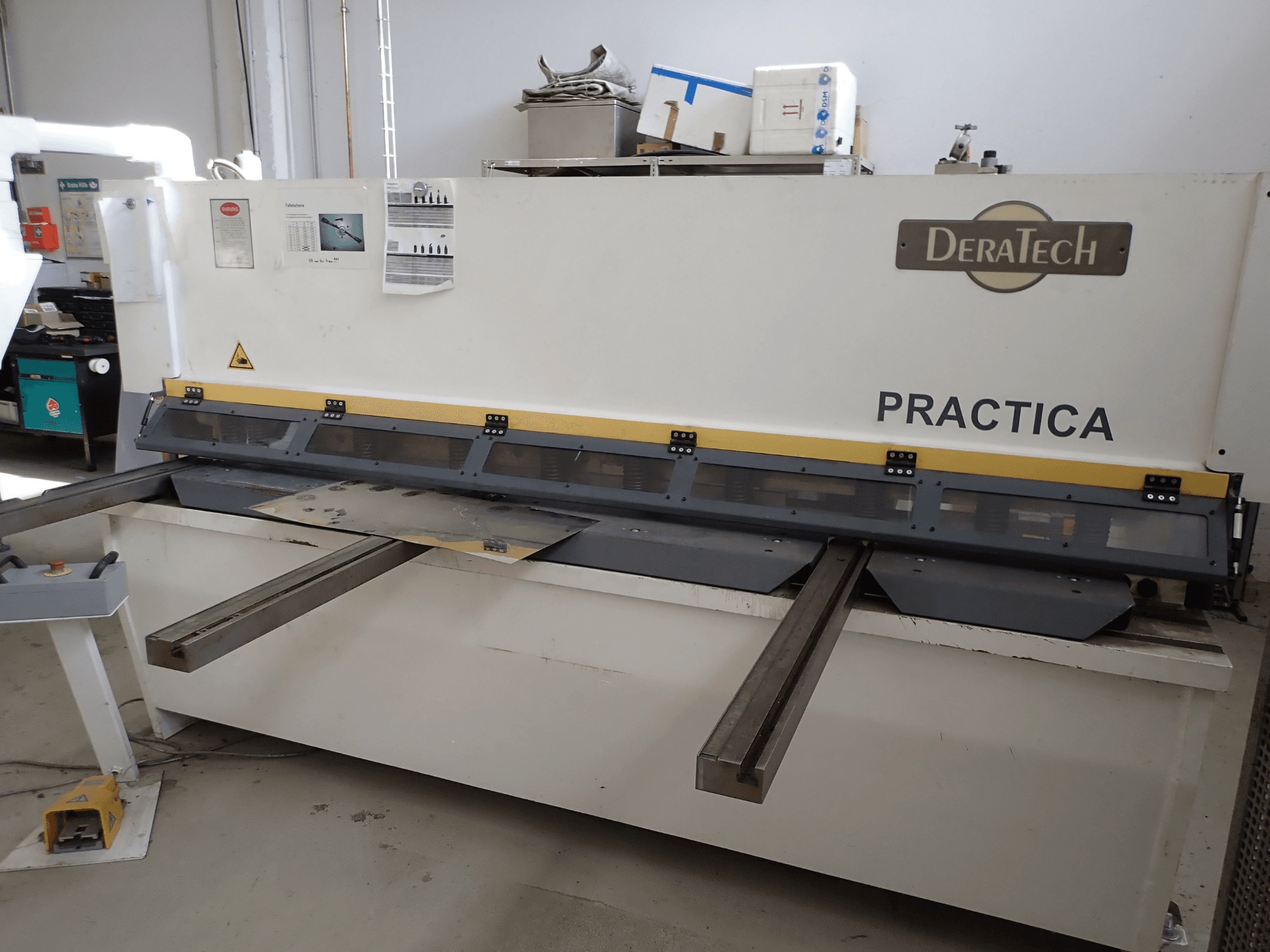 DERATECH Practica CNC-Schneidemaschine, Vorderansicht, mit Schneidmesser und Blechen auf der Arbeitsfläche.