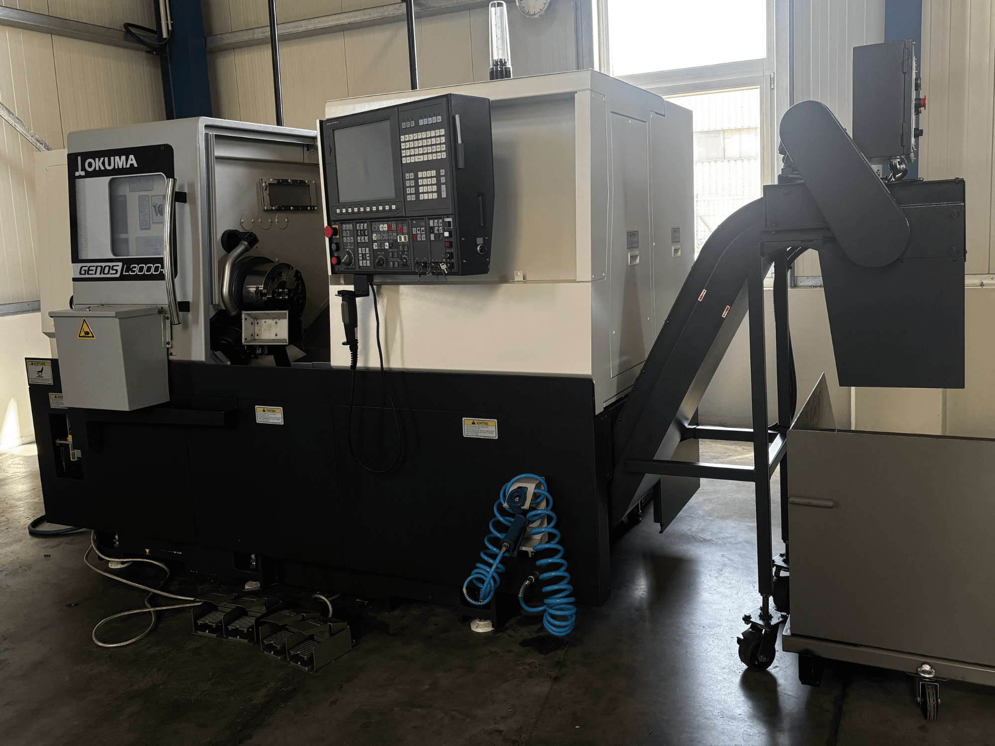 Okuma GENOS L3000-e Horizontal-Drehmaschine, Vorderansicht, mit Bedienfeld, Förderband und sichtbarem Spindelbereich.