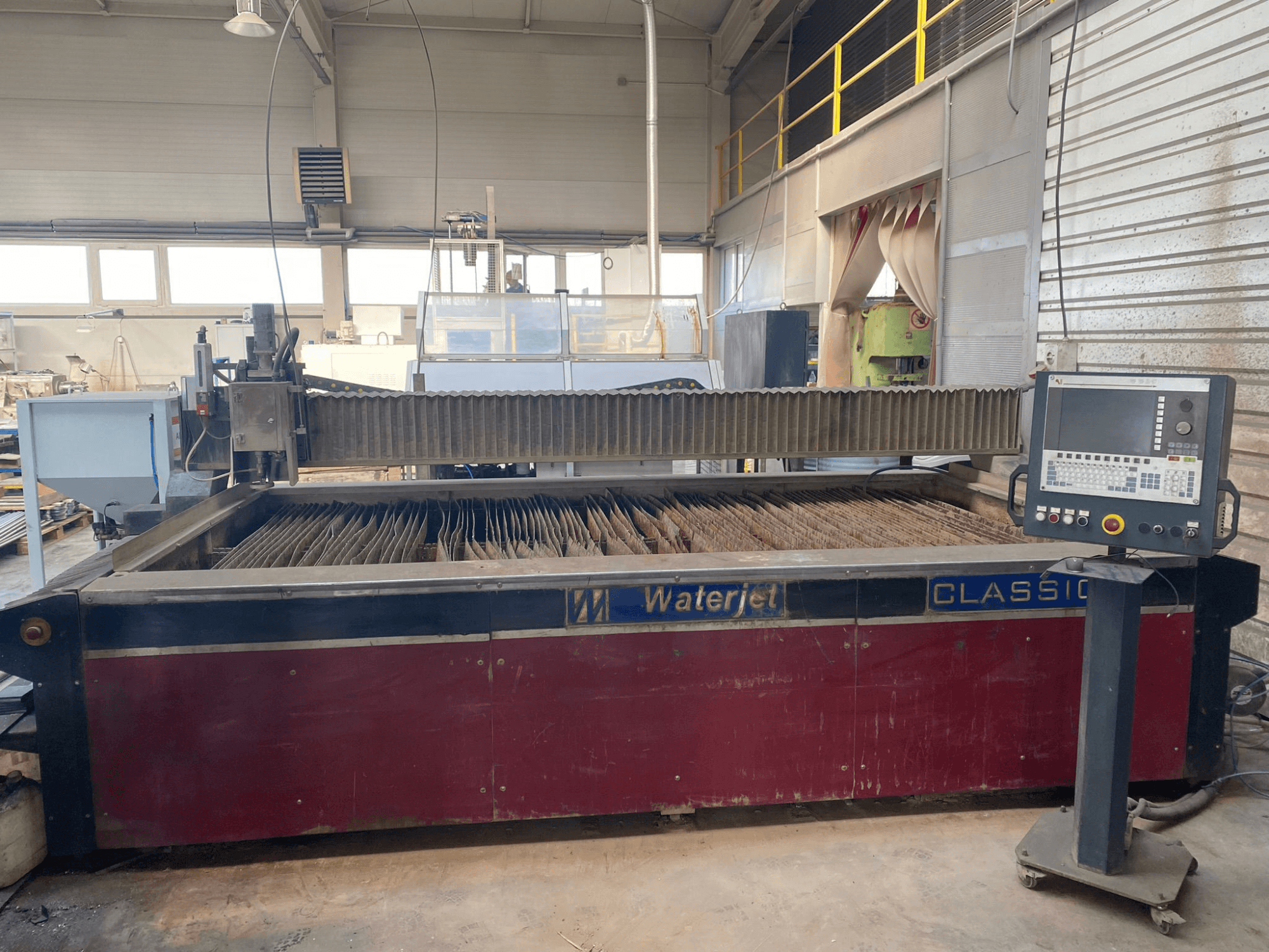 Wasserstrahlschneidmaschine CLASSIC, Vorderansicht, mit Wassertank, Bedienfeld und mehreren Metallschneidköpfen im Inneren.
