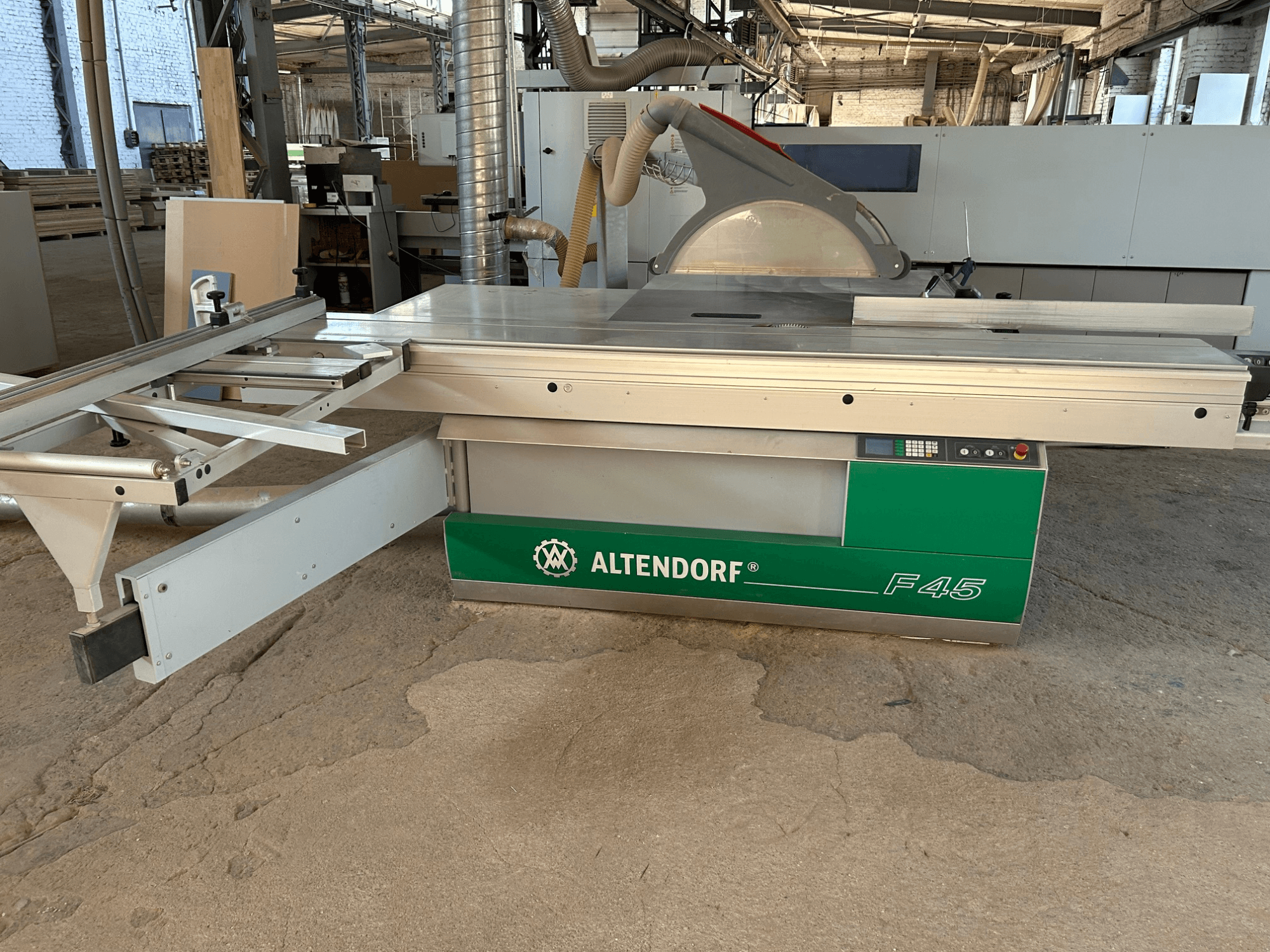 Altendorf F 45 Plattensäge, Vorderansicht, mit Sicht auf den Schneidetisch, den Sägeblattschutz und das Bedienfeld an der grün-grauen Maschine.