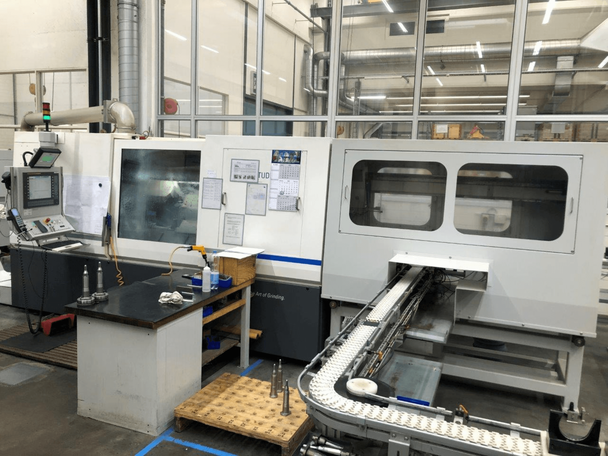 CNC-Schleifmaschine mit Bedienpult, Vorderansicht; verfügt über ein Förderband und klare Sichtfenster, die Präzisionswerkzeuge zeigen.