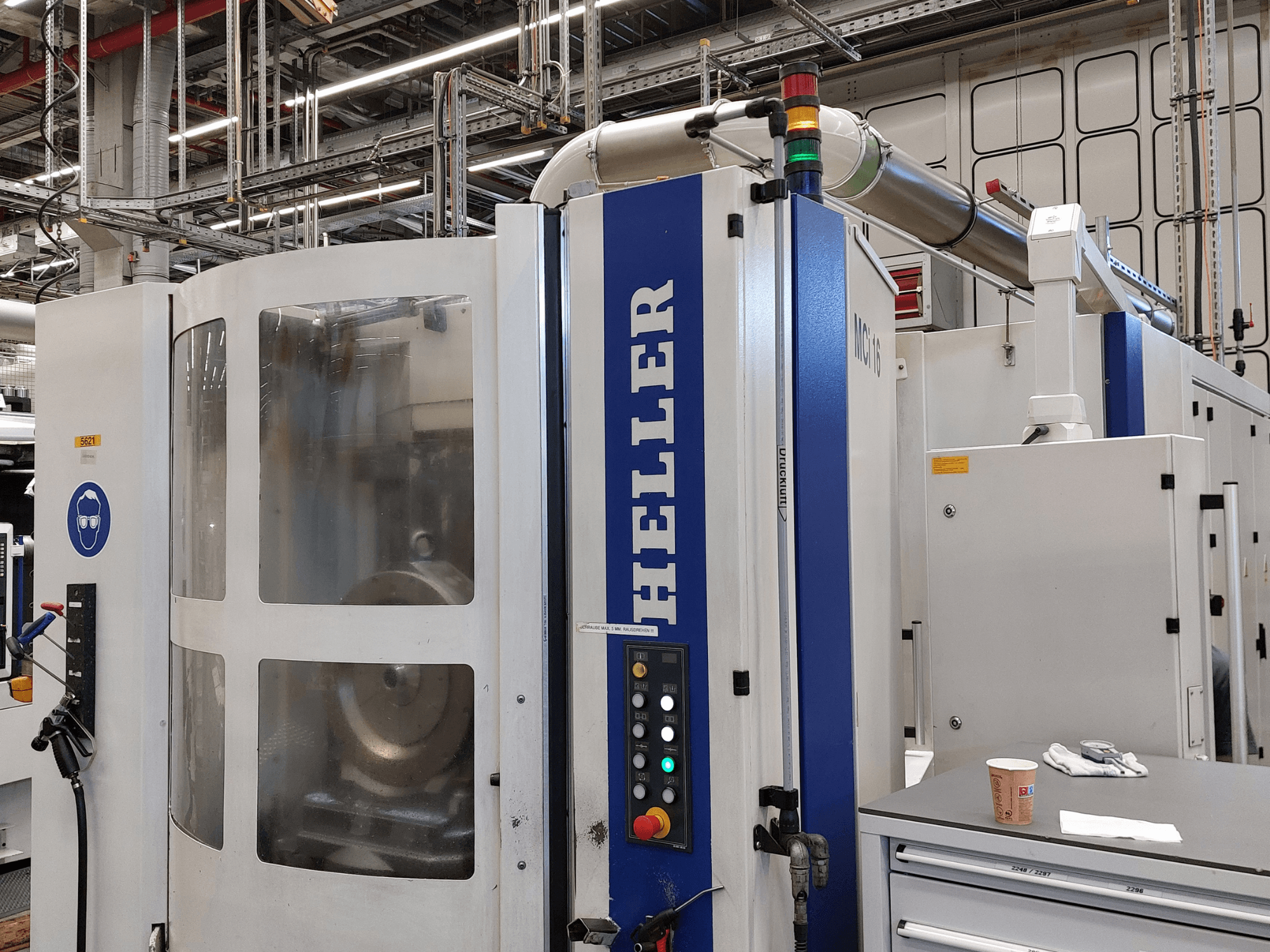 Vertikales Bearbeitungszentrum Heller MCI 16 in einer Fabrikumgebung, mit Bedienfeld und Sicherheitsbeschilderung.