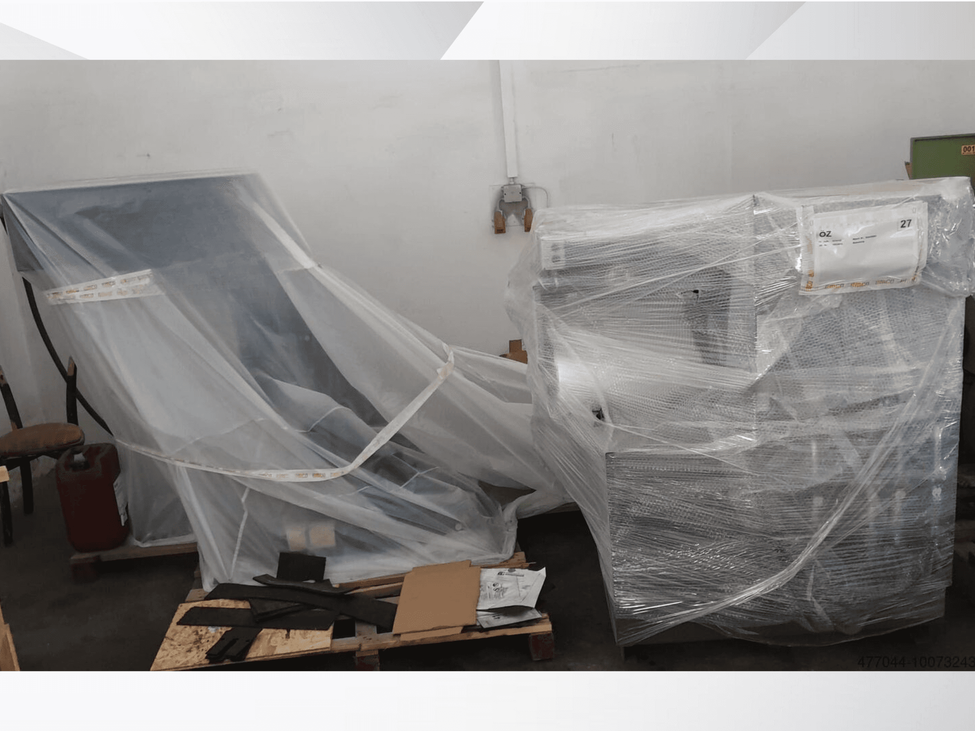 In Plastik verpackte Industrieausrüstung mit einem Stuhl und einer Maschine, von der Seite gesehen in einem Lagerhaus.