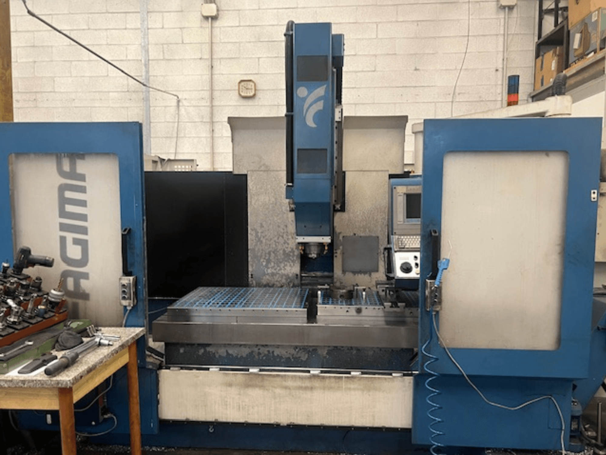 Frontansicht einer JAGIMA-CNC-Maschine mit einem großen Metallarbeitsbereich, einem sichtbaren Bedienfeld und Werkzeugen auf einem Tisch in der Nähe.