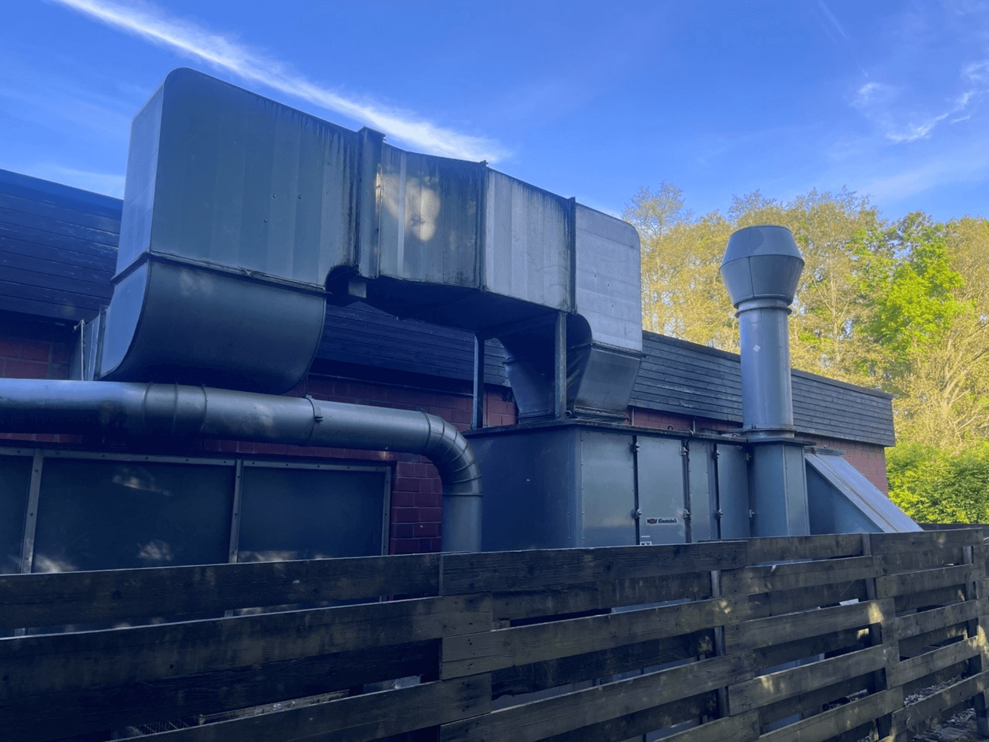 Industrielüftungsanlage mit Metallkanälen, Seitenansicht; umfasst einen quadratischen und einen zylindrischen Schornstein, grün lackiert.