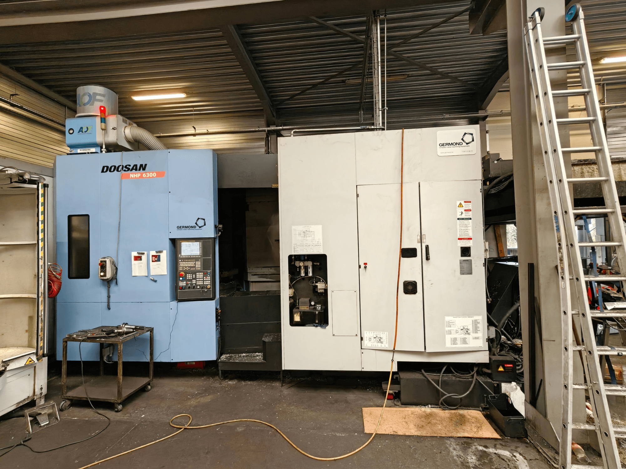 Das horizontale Bearbeitungszentrum DOOSAN NHP6300 in der Vorderansicht, mit Blick auf das Bedienfeld und die angrenzenden Maschinen in einer Werkstattumgebung.