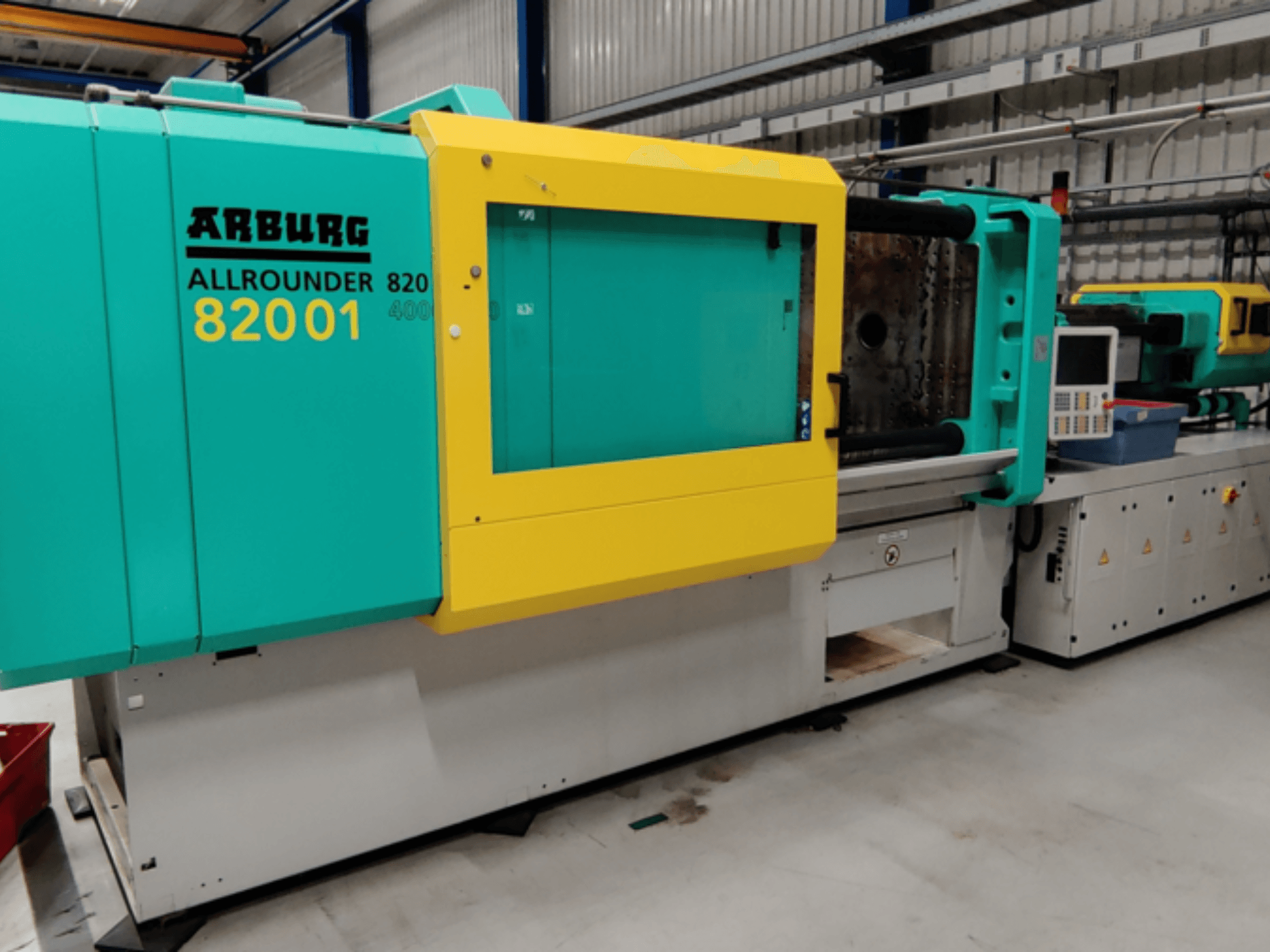 Arburg ALLROUNDER 82001 Spritzgießmaschine in den Farben Teal und Gelb, Seitenansicht mit Bedienfeld und Bedienelementen.