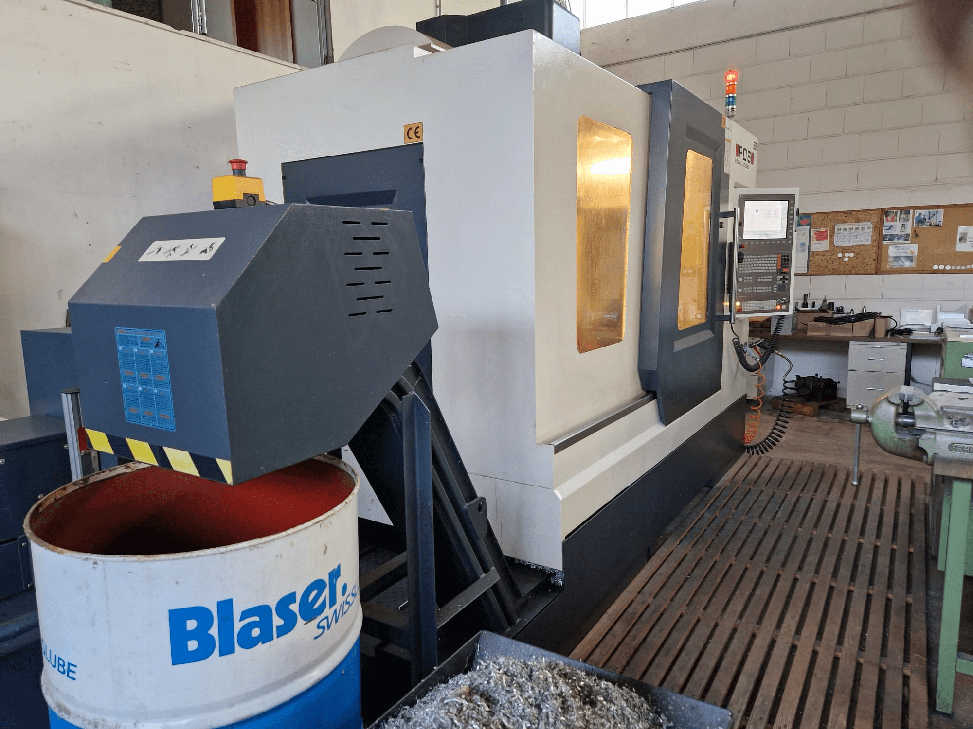 Frontansicht des vertikalen Bearbeitungszentrums POSmill C 1050, mit Kühlmittelanlage über der Blaser-Trommel und Bedienfeld.