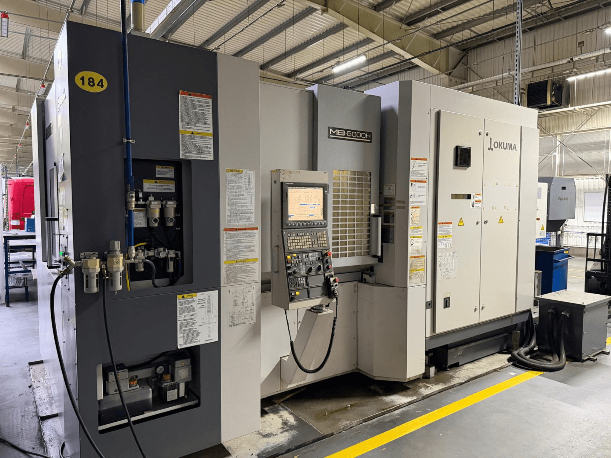 Okuma MB 5000H Horizontal-Bearbeitungszentrum in der Frontansicht, mit Bedienelementen, Beschriftung und hydraulischen Anschlüssen.