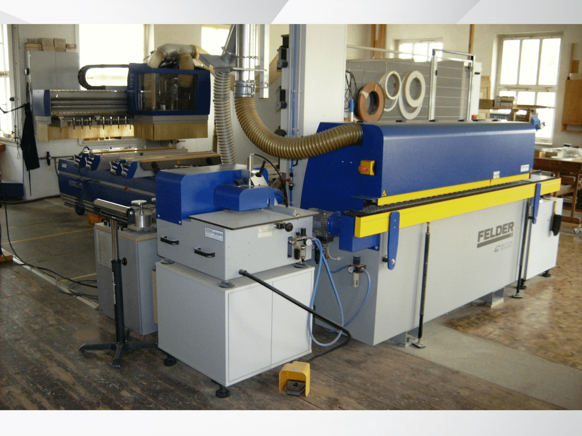 FELDER G500 Kantenanleimmaschine in einer Werkstatt, Seitenansicht, die die blau-gelbe Konstruktion mit Bedienelementen und Abluftkanälen zeigt.