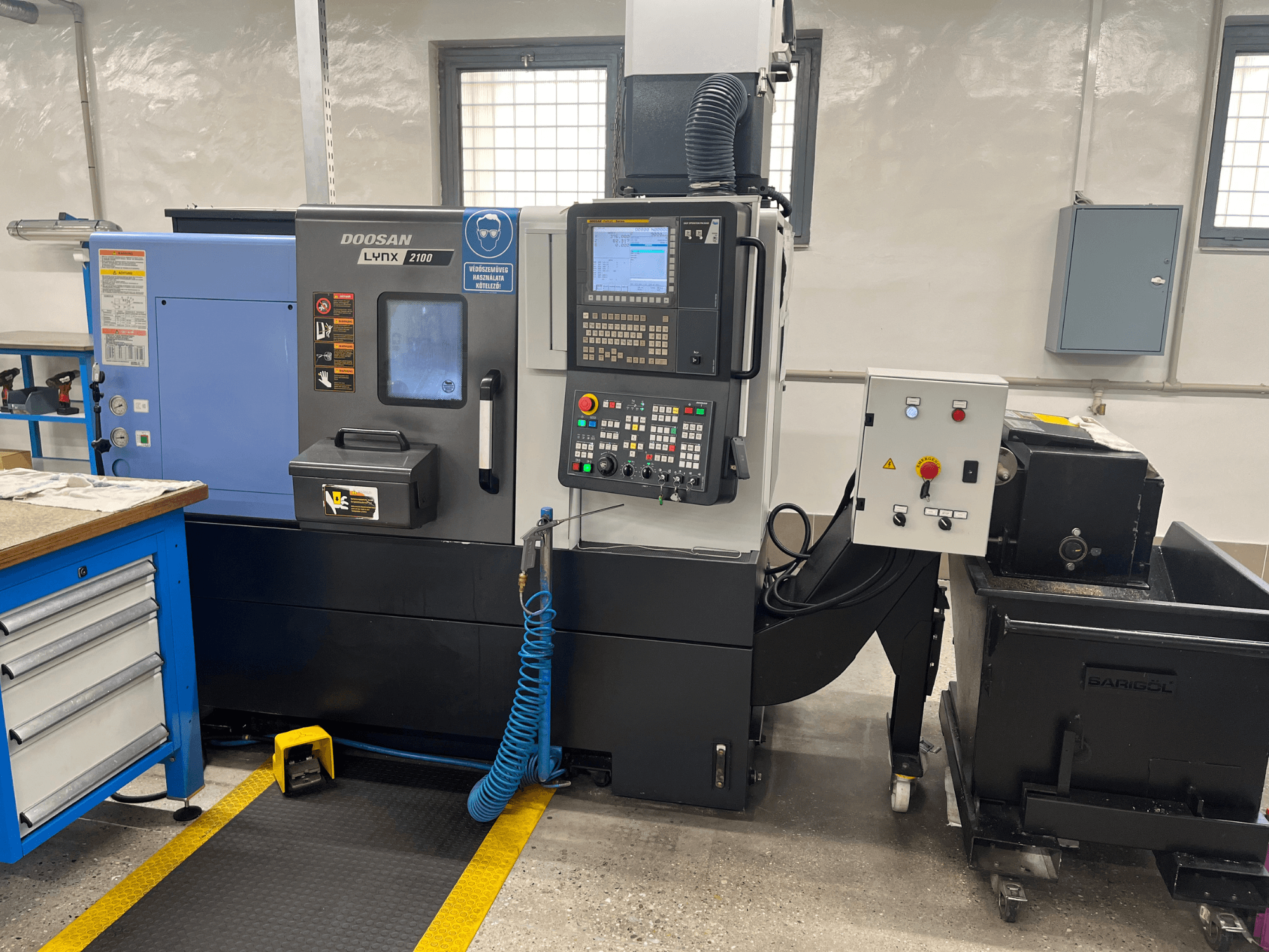 Doosan Lynx 210 Drehmaschine in der Werkstatt, mit Bedienfeld, Werkzeugspeicher und Kühlmittelsystem, Seitenansicht mit Details zum Arbeitsbereich.