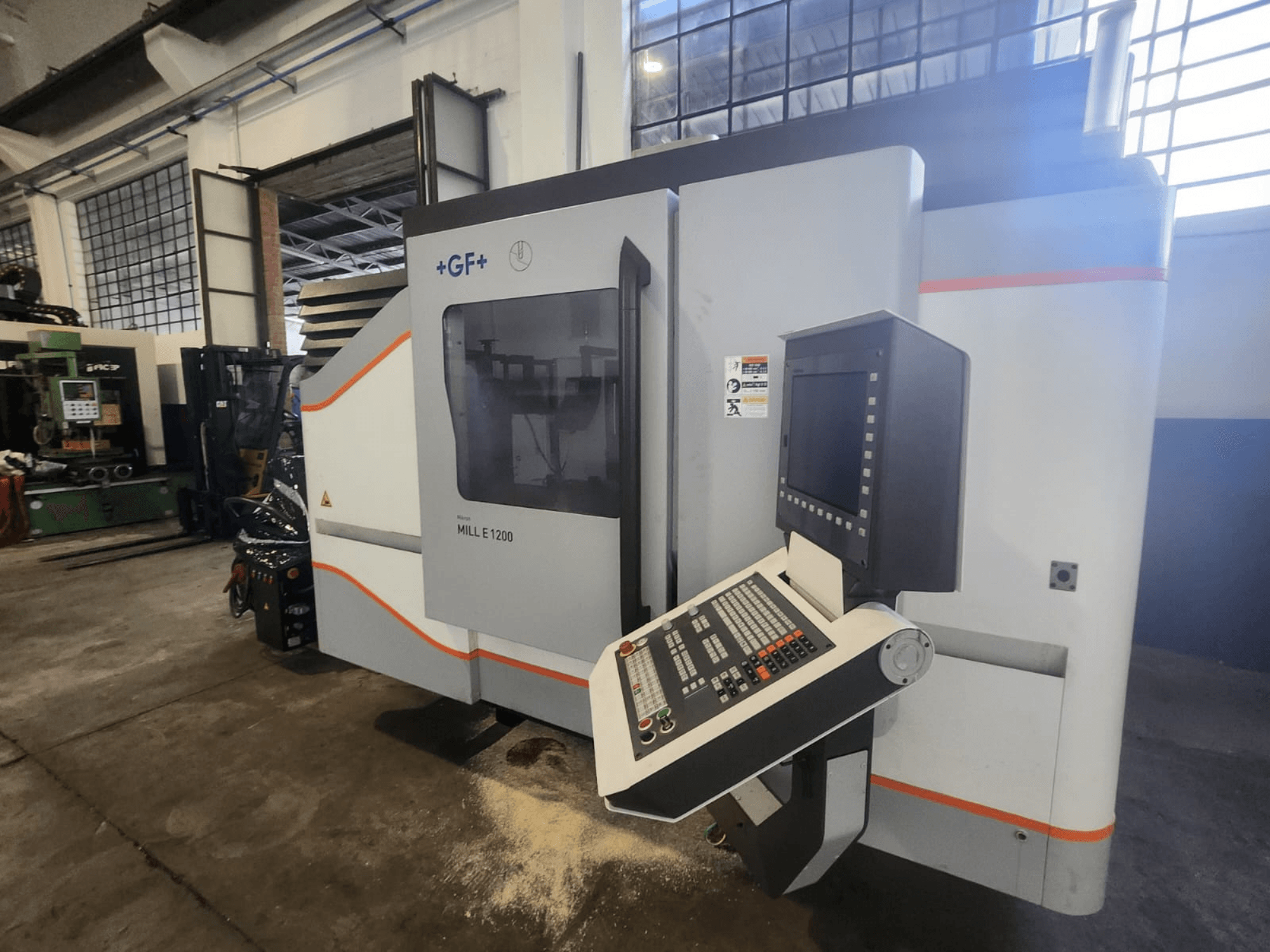 GF MILL E1200, Frontansicht der Fräsmaschine mit Bedienfeld, Bildschirm und Sicherheitsschildern, in Werkstattumgebung.