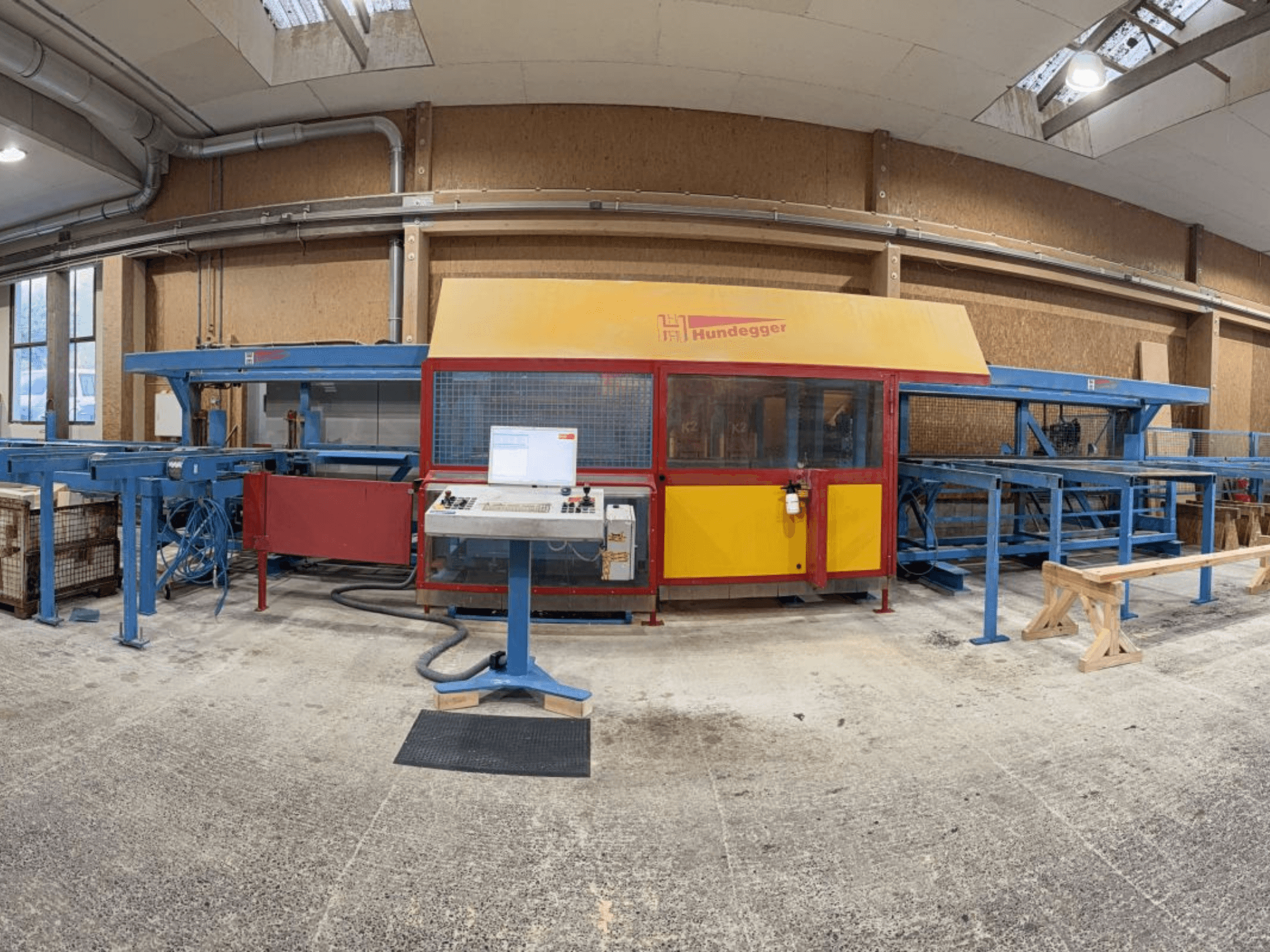 Frontansicht der kompletten Holzproduktionslinie HUNDEGGER K2-4-450 mit Schaltschrank und Förderanlage.