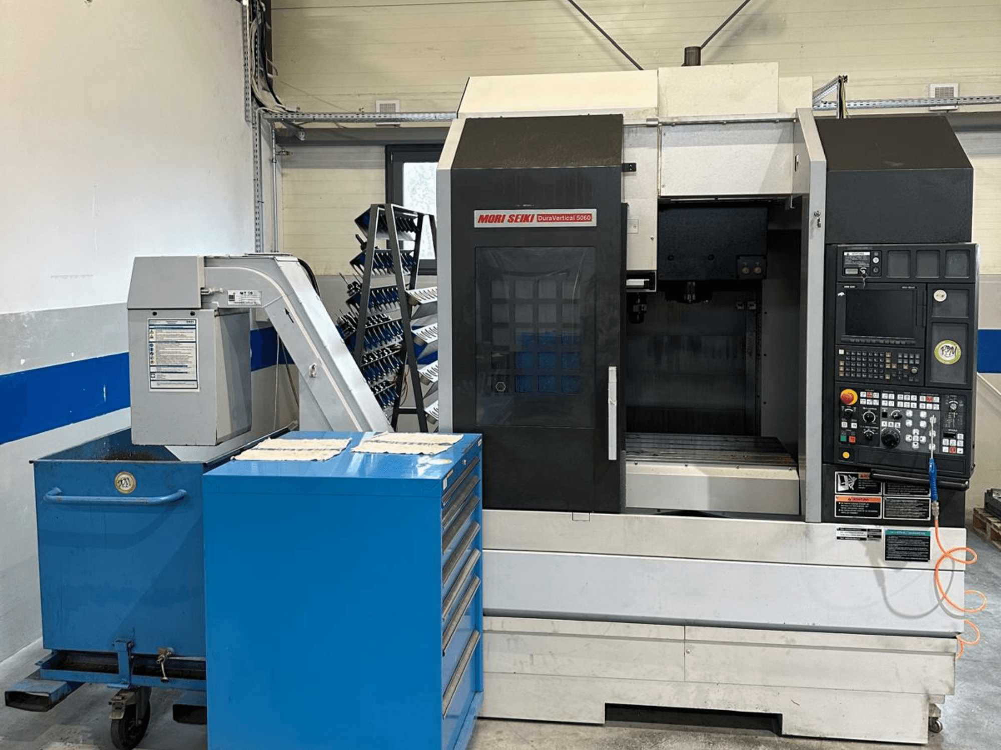 MORI SEIKI DURA VERTICAL 5060, Vorderansicht eines vertikalen Bearbeitungszentrums mit Bedienfeld und angrenzendem Werkzeugmagazin.