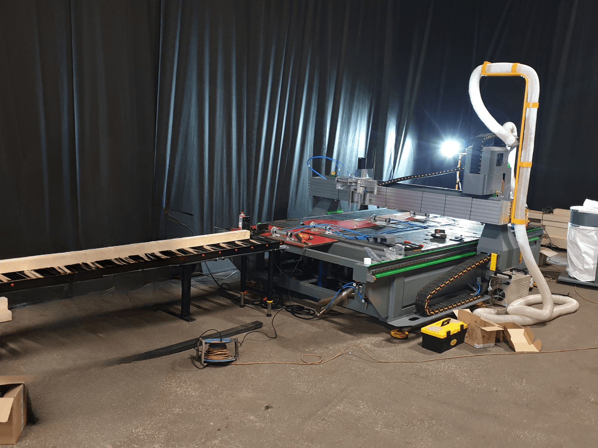 CNC-Maschine mit seitlichem Förderband, Werkzeugen auf dem Tisch und Kanal für die Staubabsaugung. Schwarzer Hintergrund, Vorderansicht.