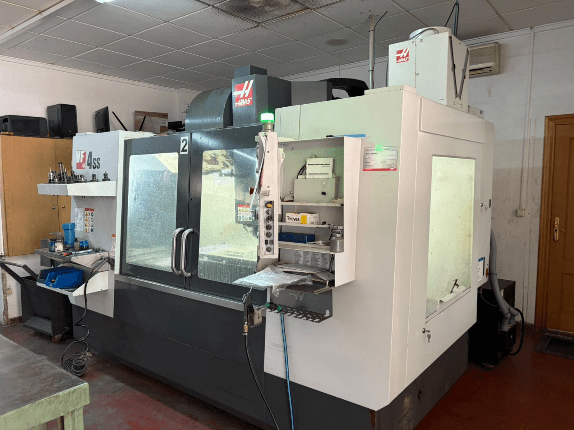 Vertikales Bearbeitungszentrum HAAS VF 4SS in einer Werkstatt, Vorderansicht, mit Blick auf das Bedienfeld und den Arbeitsbereich mit Werkzeugen und Materialien.