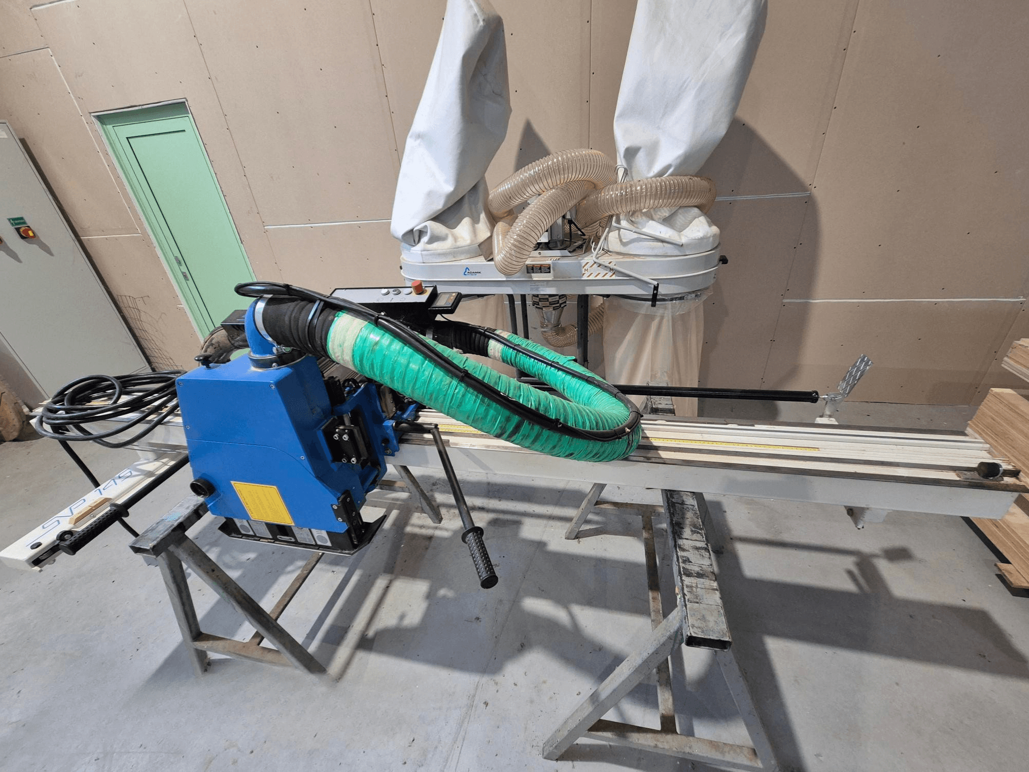 Blaue horizontale Plattensäge SVP-175 mit grünem Staubschlauch und Halterung, von der Seite gesehen in einer Werkstatt.