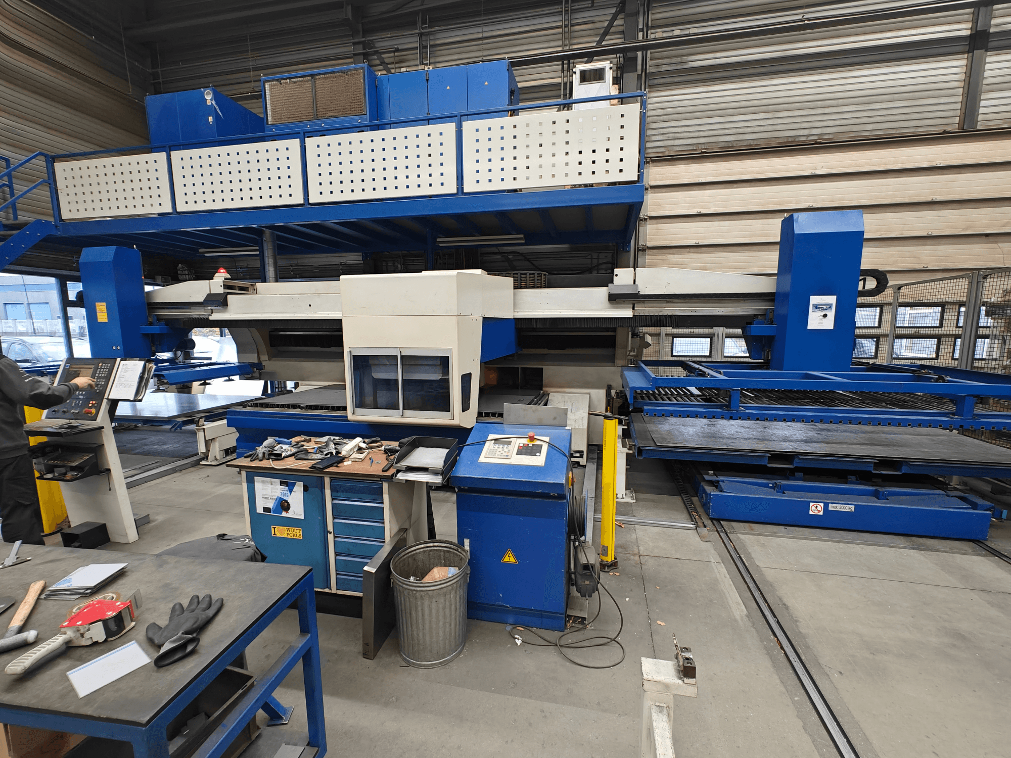 Industrielle CNC-Maschine aus der Vorderansicht, mit blau-weißer Konstruktion, Bedienfeld und verschiedenen Werkzeugen auf dem Arbeitstisch.