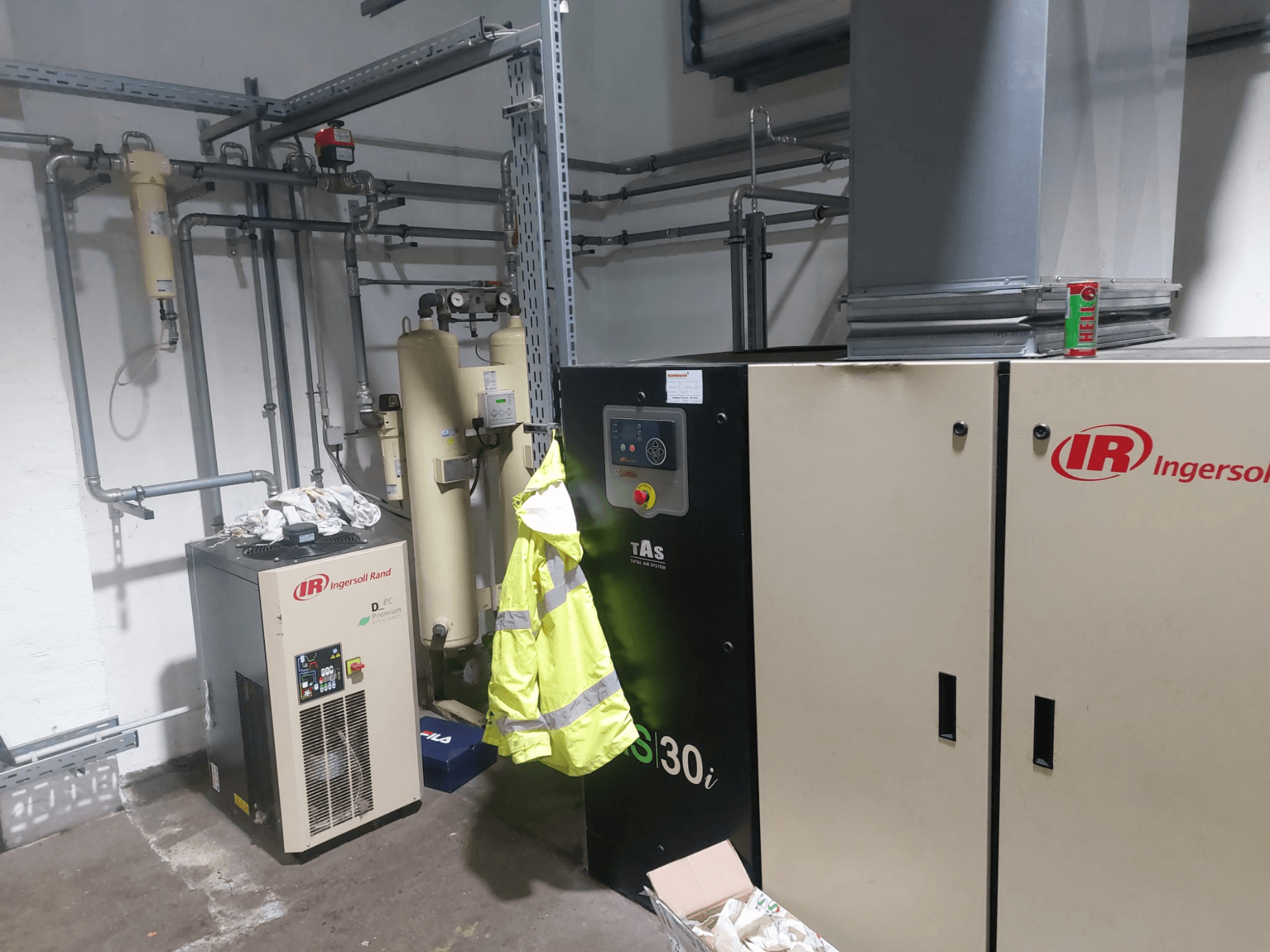 Eine Werkzeugmaschine vom Typ Ingersoll Rand D480EC-A in einer Werkstatt, Seitenansicht mit Rohrleitungen, Bedienelementen und einer gelben Sicherheitsweste in der Nähe.