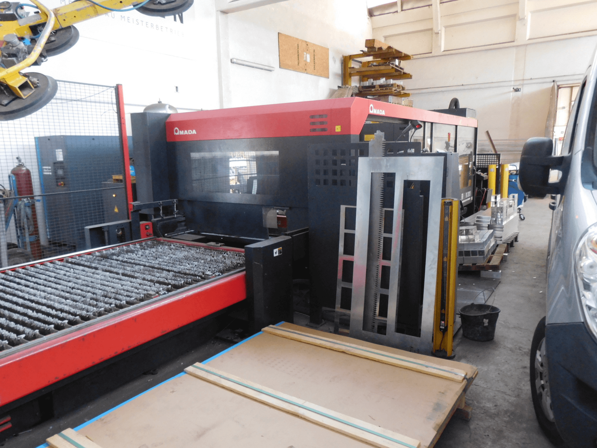 Frontansicht der AMADA FO-3015 II RI CO2-Laserschneidanlage mit Schneidbett und umliegendem Arbeitsbereich.