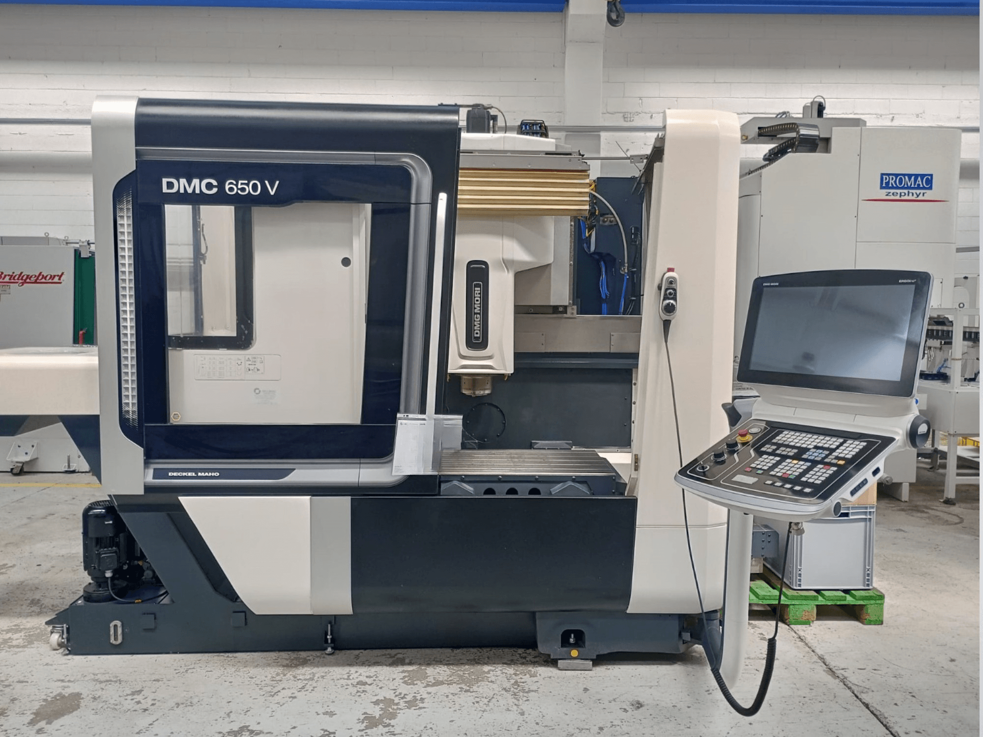 Decker Maho DMC 650 V CNC-Maschine in der Seitenansicht, mit einem Bedienfeld mit Tasten und einem Bildschirm, in einer industriellen Umgebung.