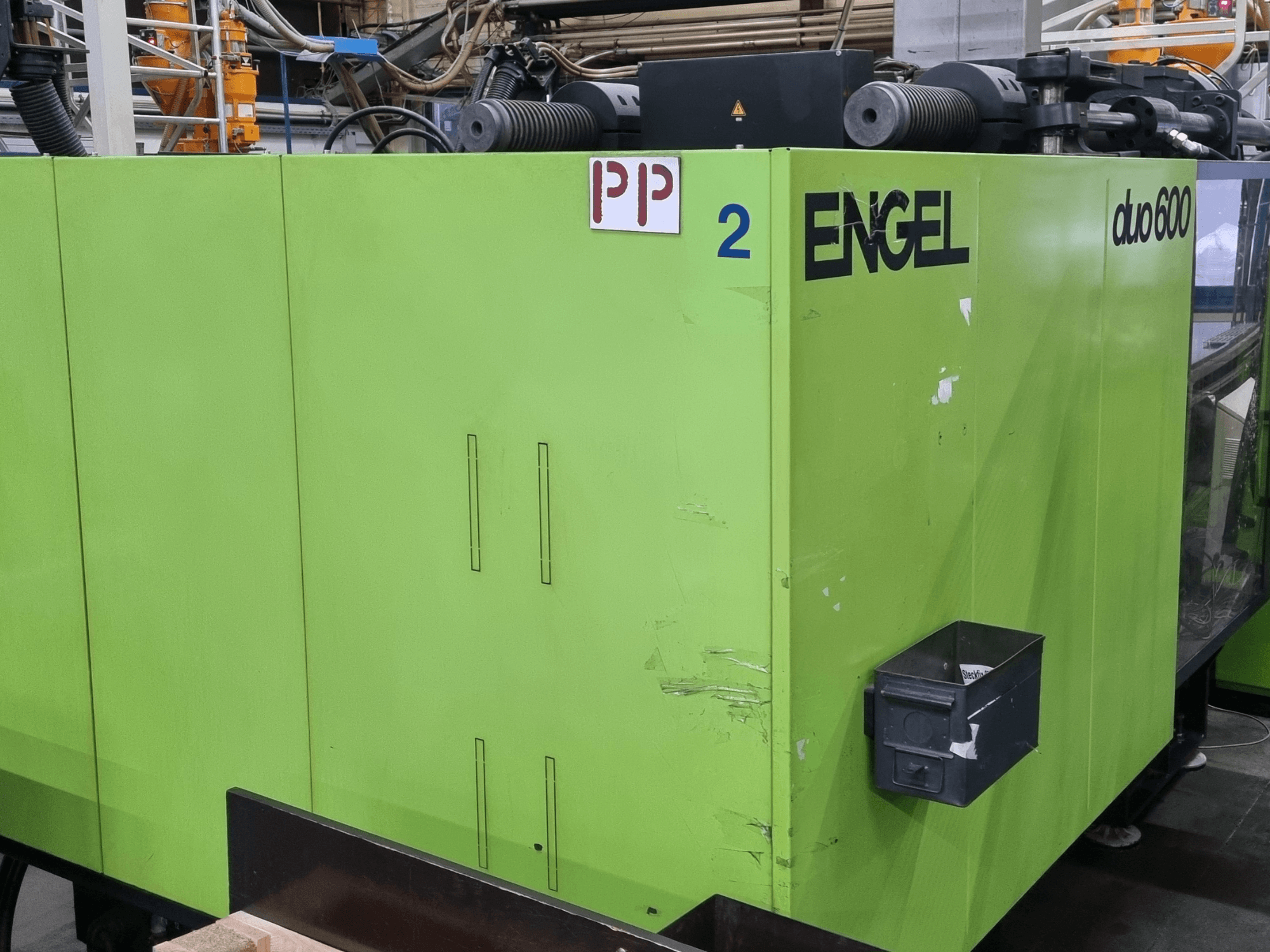 Hydraulische Spritzgießmaschine Engel Duo 600, grüne Außenfarbe, Vorderansicht, mit beschrifteten Bauteilen und Materialaufbewahrungsbox.