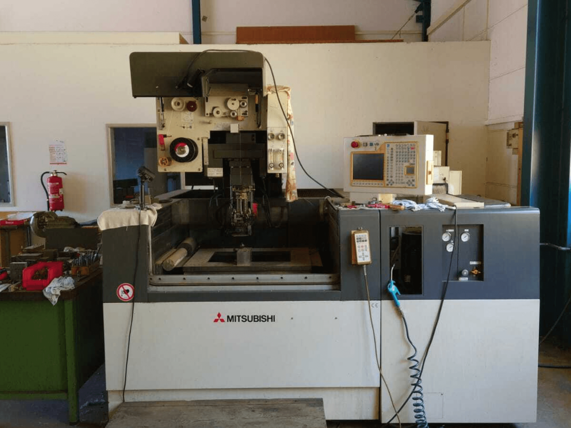 Vorderansicht der Mitsubishi FA20-Drahterodiermaschine mit sichtbarem Bedienfeld, Arbeitsbereich und Sicherheitsbeschilderung.