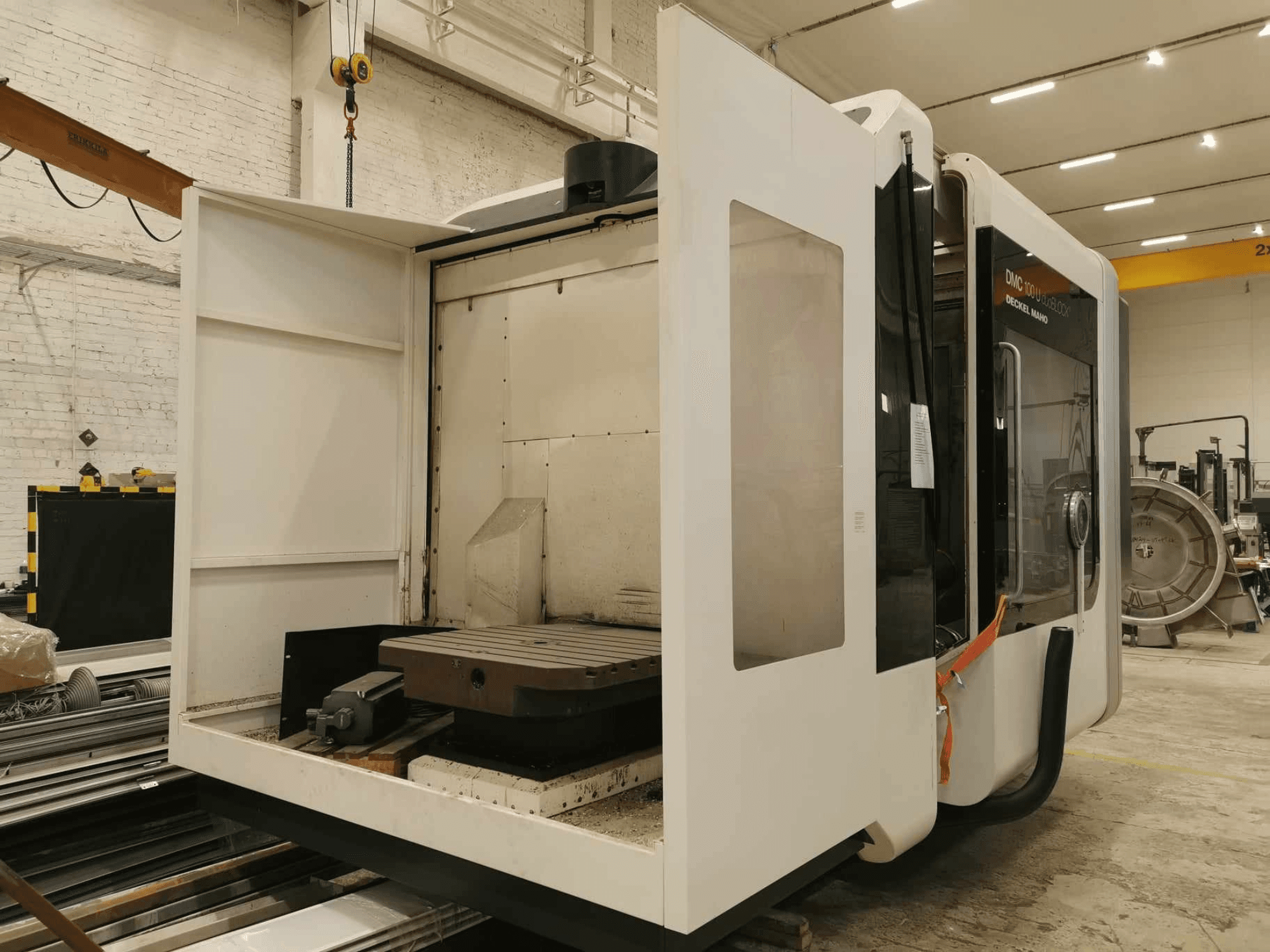 DMC 100U lineare CNC-Maschine, Seitenansicht mit geöffneter Zugangstür, zeigt Arbeitstisch und interne Komponenten.