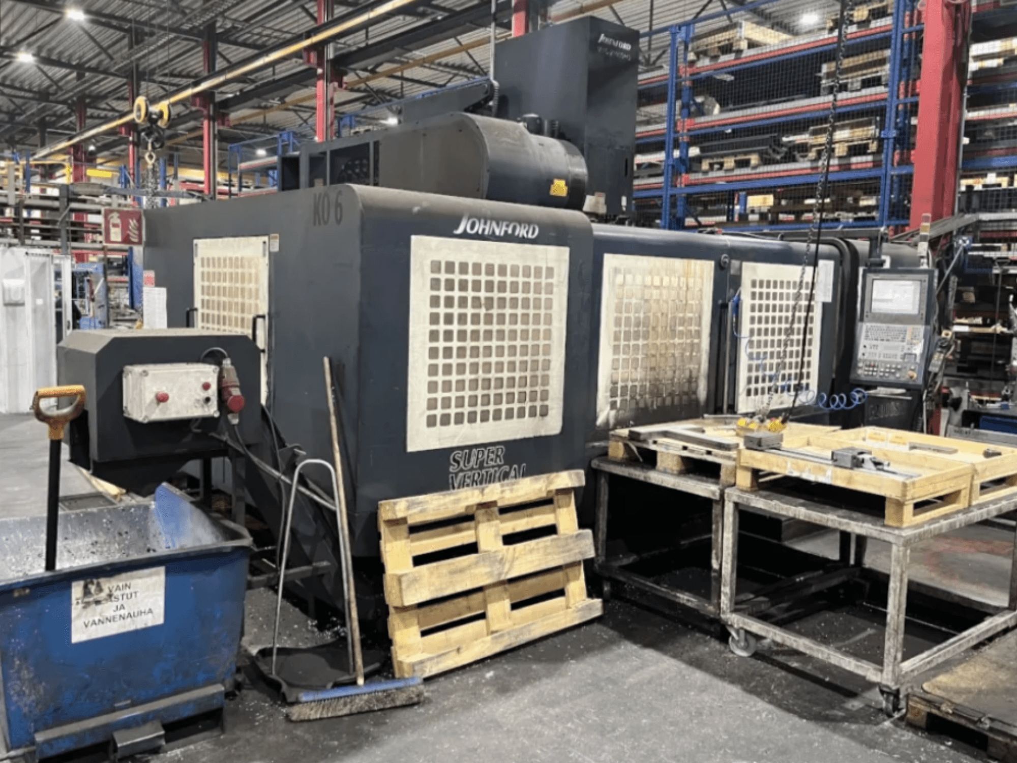 Johnford Super Vertical Fräsmaschine in einer Fabrik, Seitenansicht mit Bedienfeld, Paletten und Reinigungsgeräten in der Nähe.