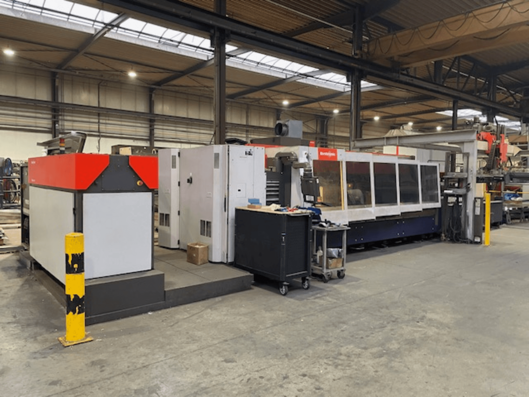 Bystronic BySpeed 3015 CO2-Laserschneidanlage, Seitenansicht in einer Werkstatt, mit markanten roten und grauen Designelementen.