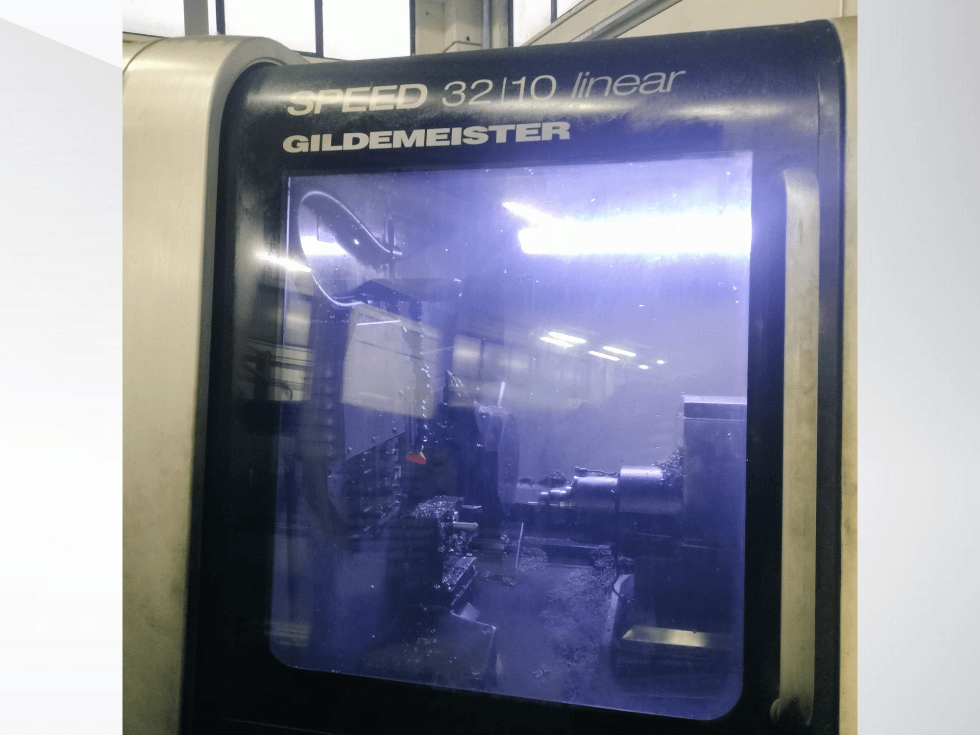 Vorderansicht der linearen CNC-Maschine SPEED 3210 von Gildemeister, die die internen Komponenten und das flüssige Kühlmittel im Betrieb zeigt.