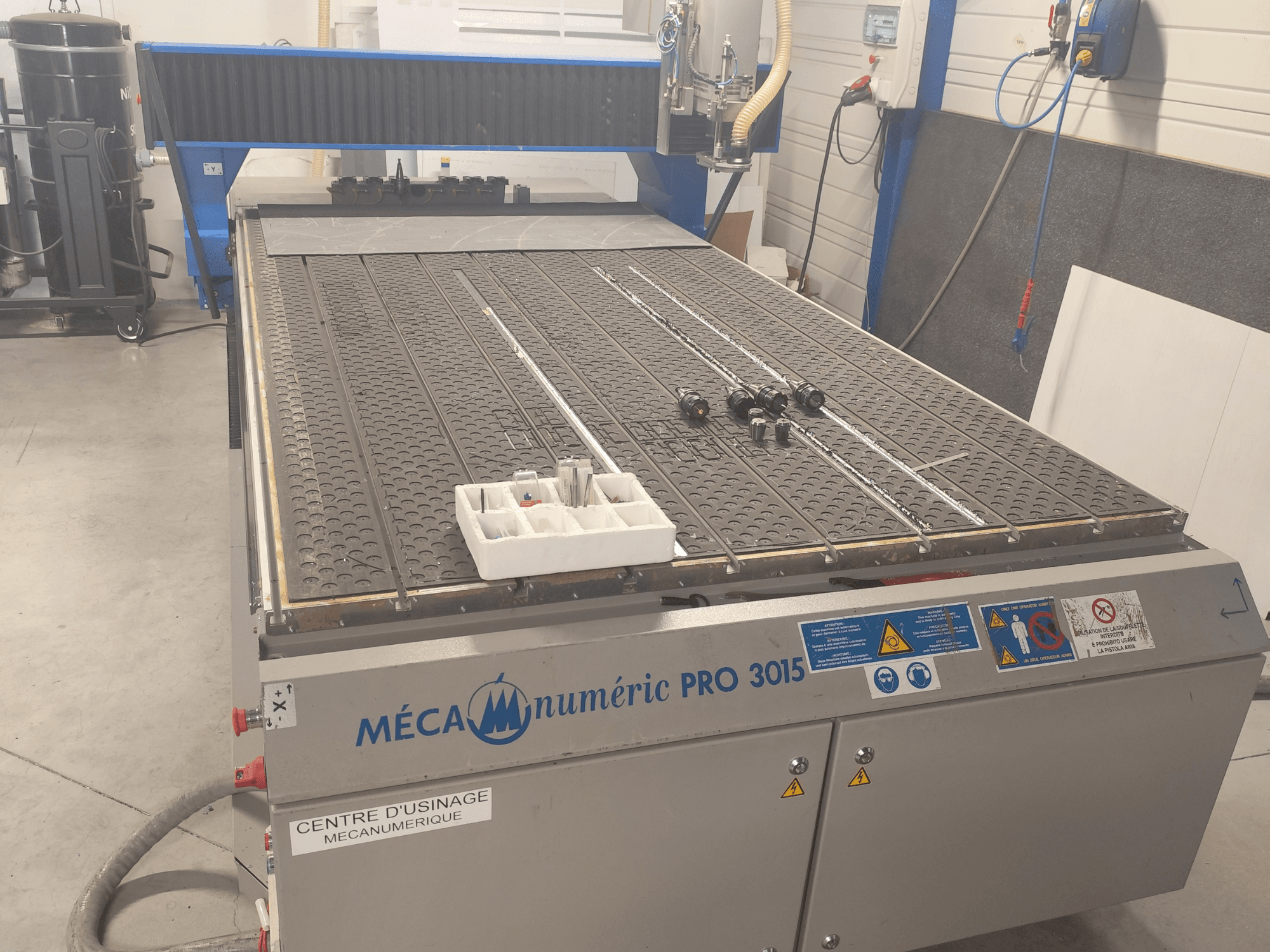 CNC-Fräse MECANUMERIC Pro 3015 in der Vorderansicht, mit detailliert dargestelltem Schneidetisch, Bedienfeld und Zubehör auf dem Tisch.