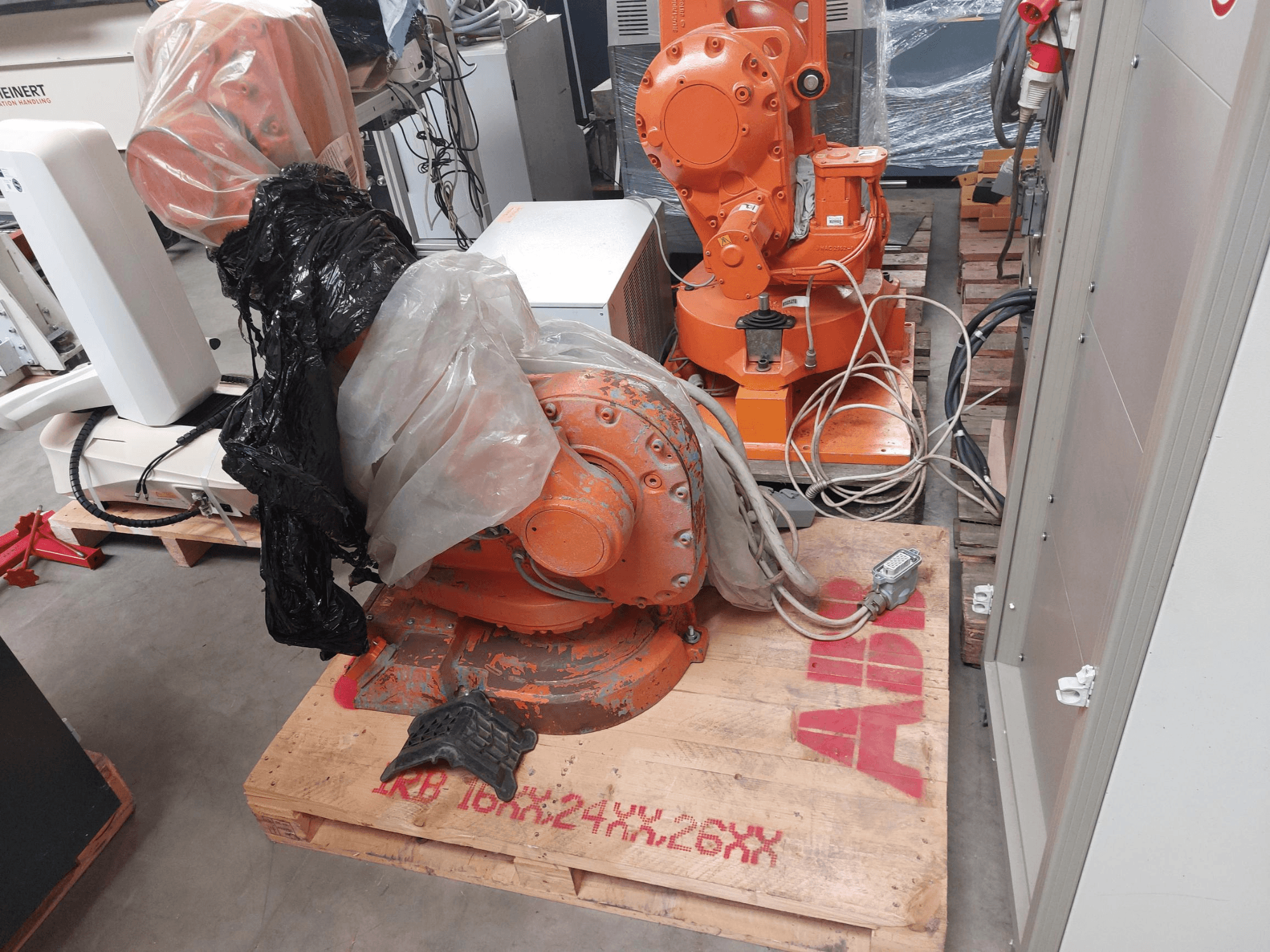 ABB IRB 1600 M2004 Roboterarm, teilweise mit Kunststoff bedeckt, von vorne gesehen, mit Kabeln und zusätzlichen Maschinen in der Nähe.