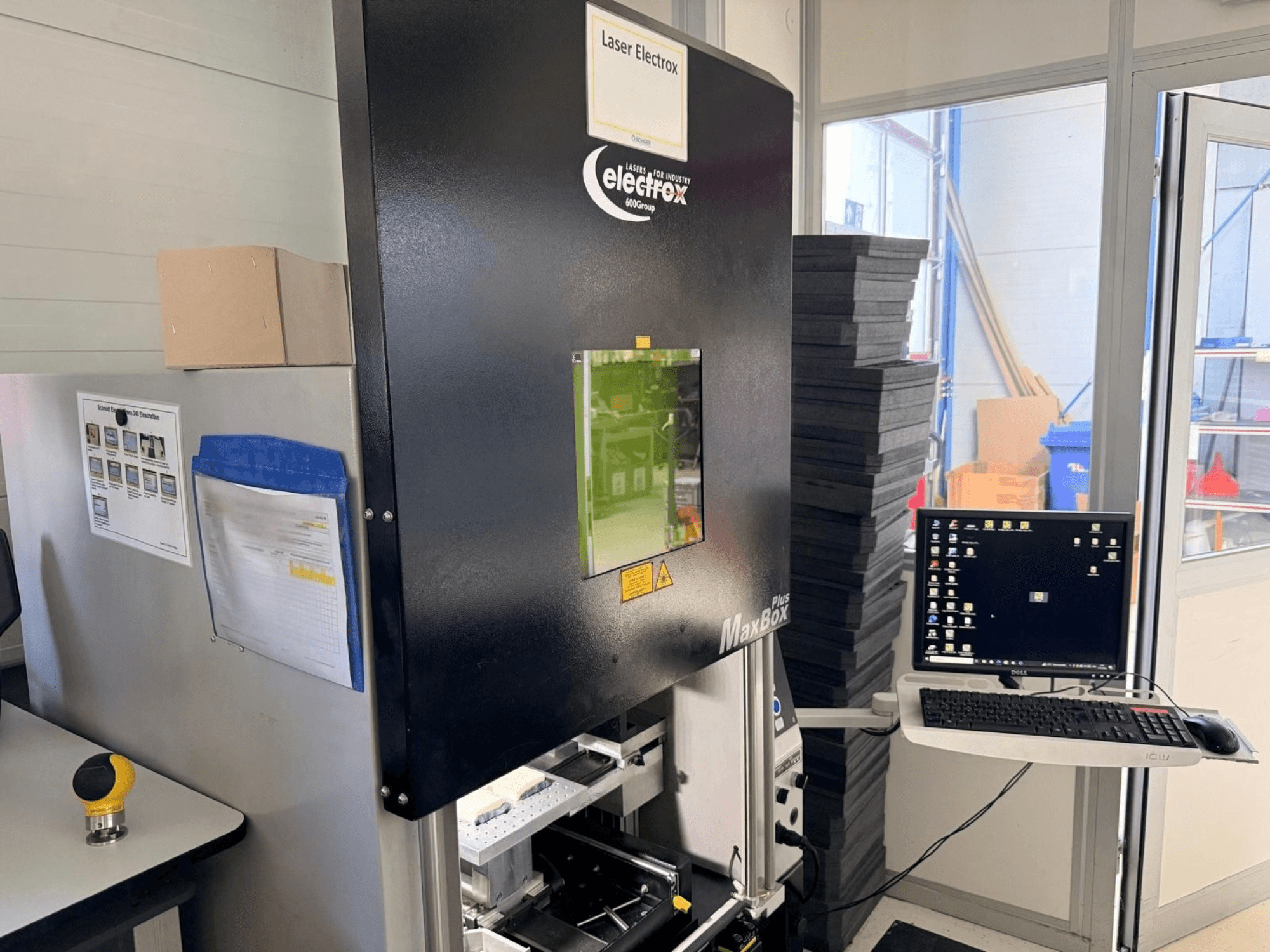 Die Laserbeschriftungsmaschine ELECTROX MaxBox Plus in Seitenansicht, mit Bedienmonitor, grünem Sichtfenster und Arbeitsbereich.