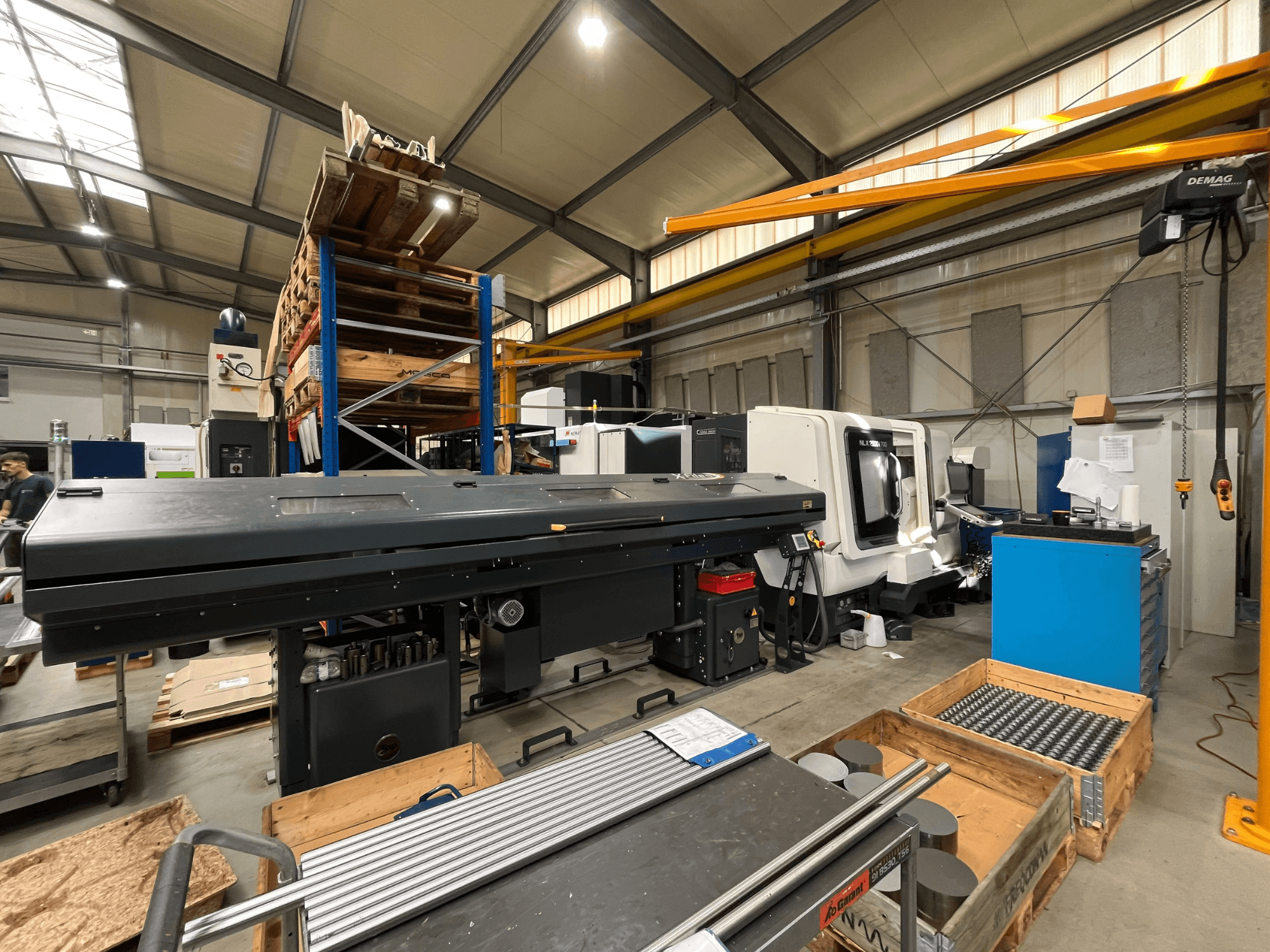 Horizontaldrehmaschine DMG MORI MORI NLX 2500/700 SY in einer Werkstatt, von der Seite gesehen, mit Lager und Werkzeugen im Hintergrund.
