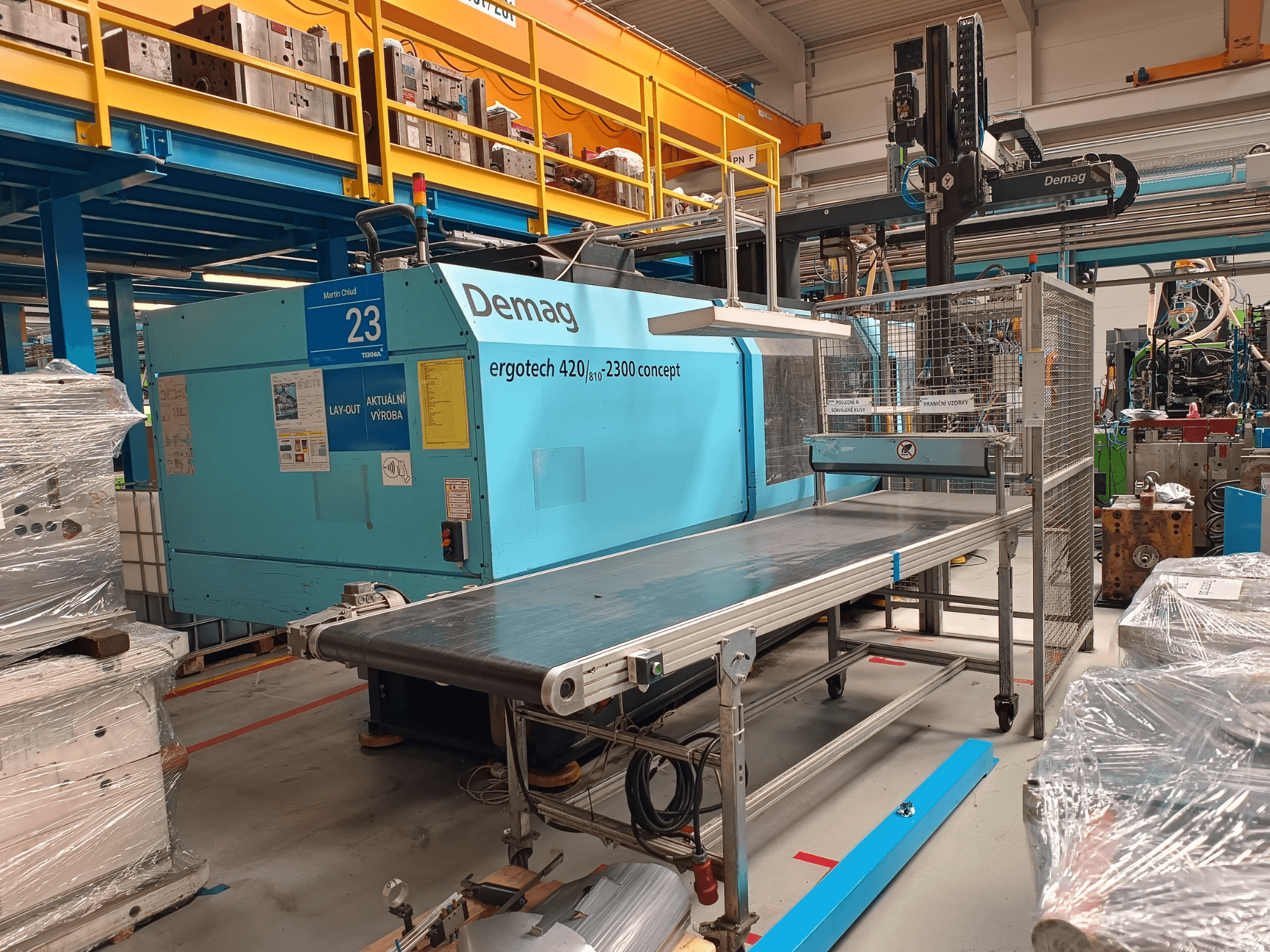 Hydraulische Spritzgießmaschine Demag ergotech 420/810 - 2300 in der Seitenansicht, mit Förderband und Schutzumhausung.
