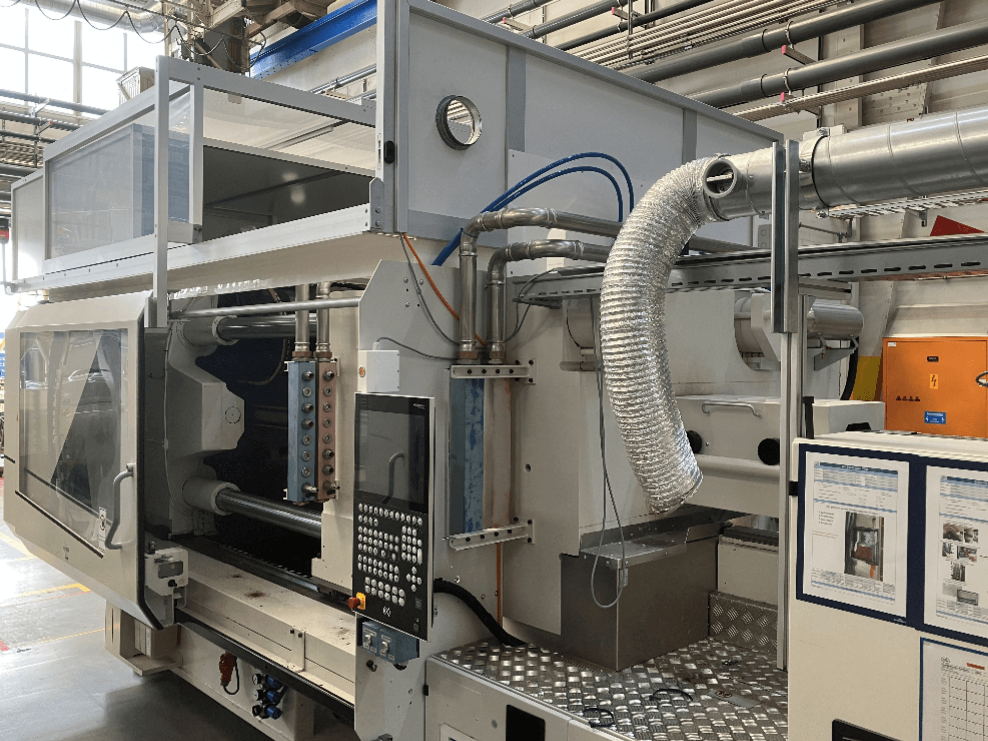 Industriemaschine von Brand X, Seitenansicht mit Bedienfeld, Rohrleitungen und Maschinenkomponenten in einer Fabrikumgebung.