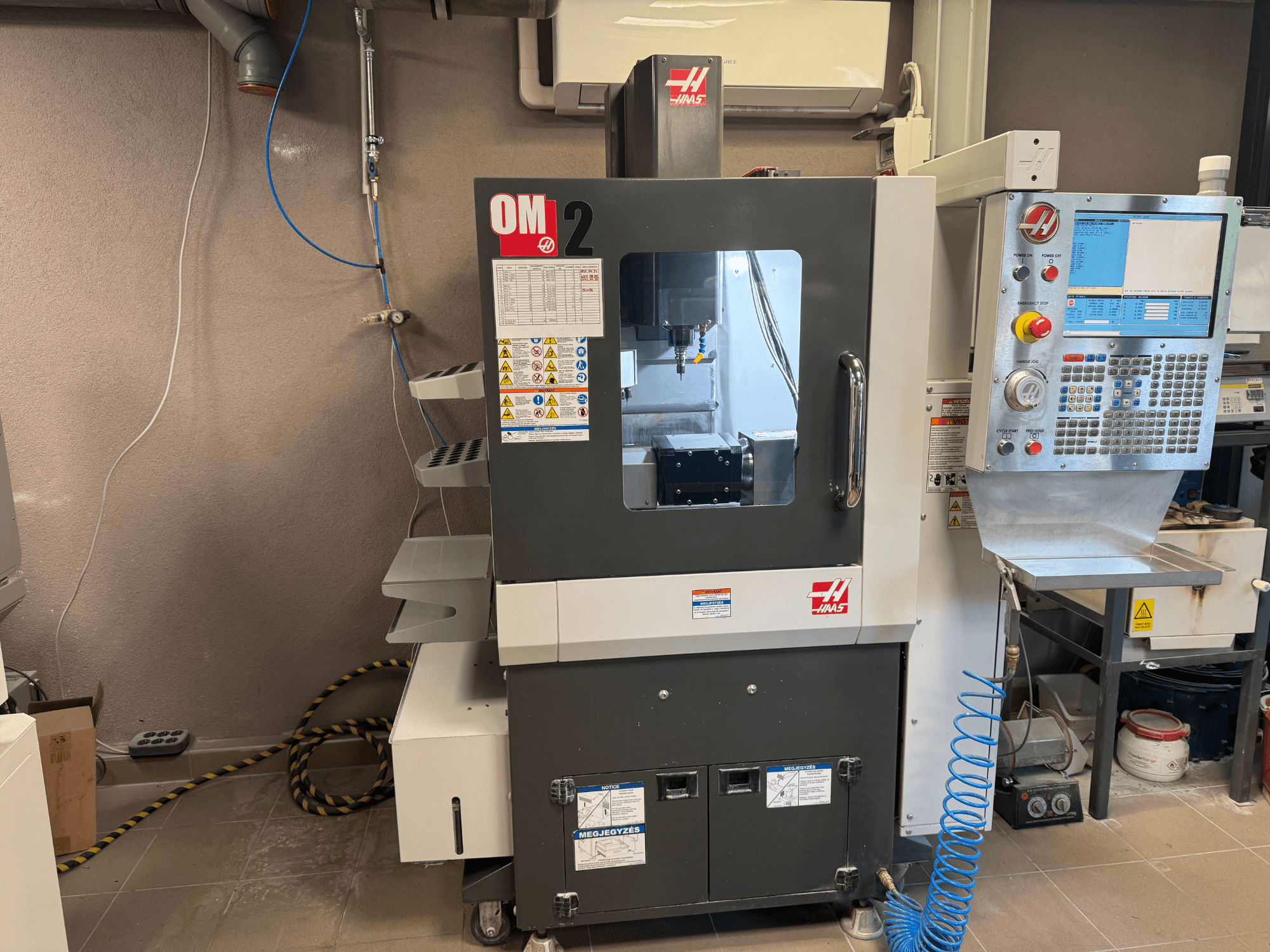 Haas OM-2 CNC-Maschine, Vorderansicht, mit Bedienfeld, Spindel und Sicherheitsschildern, aufgestellt in einer Werkstattumgebung.