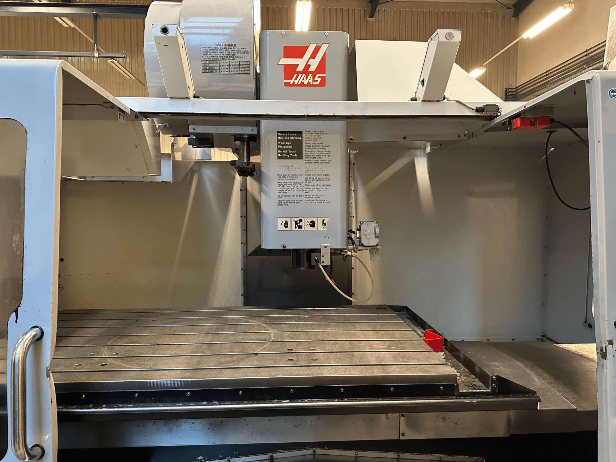 Haas CNC-Fräsmaschine, Modell VF-2, Vorderansicht mit Bedienelementen, Metallarbeitstisch und Sicherheitsaufkleber auf dem Bedienfeld.